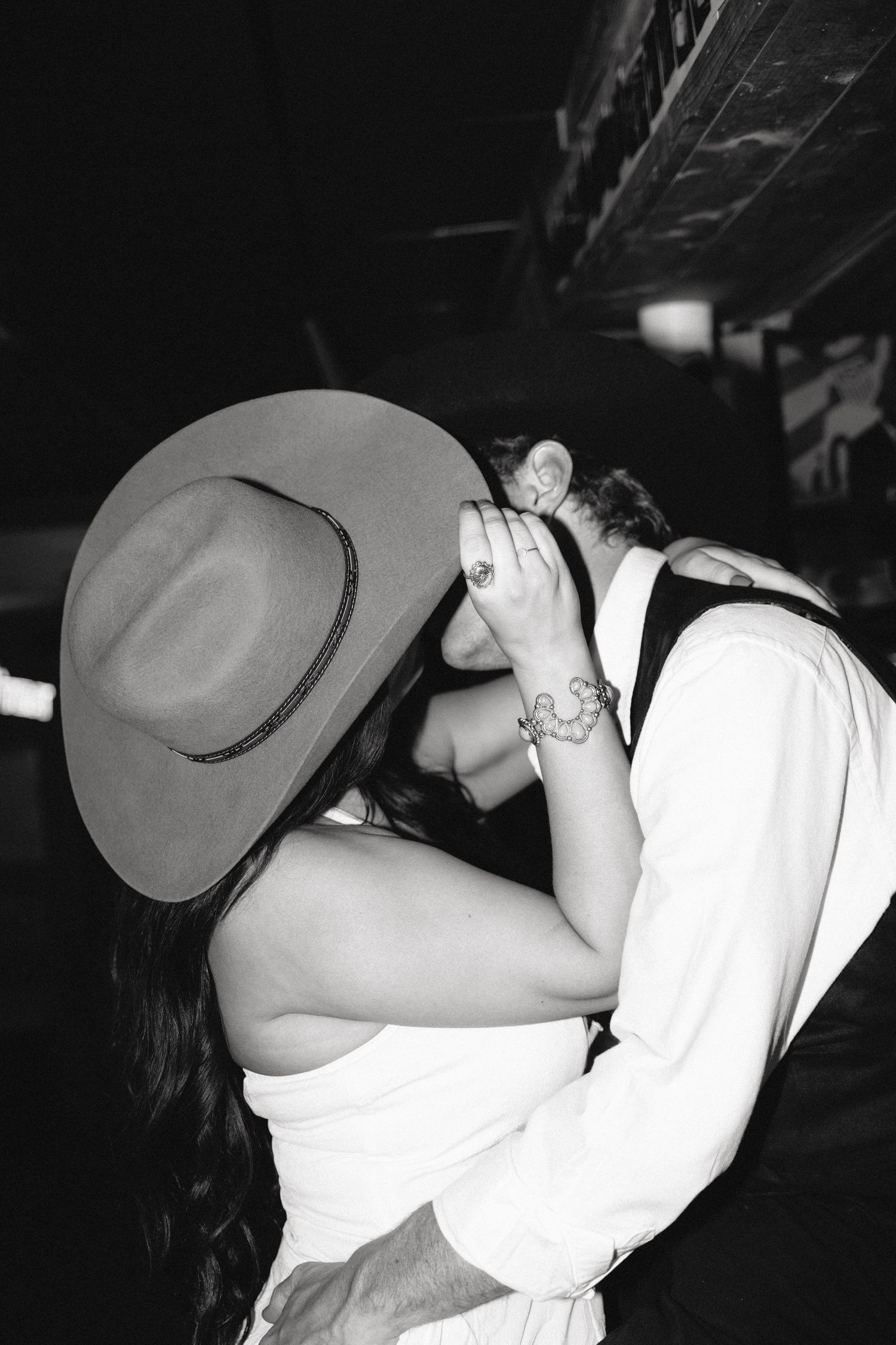 Black and white photo of a couple sharing a romantic kiss, the woman wearing a cowboy hat and white dress.
