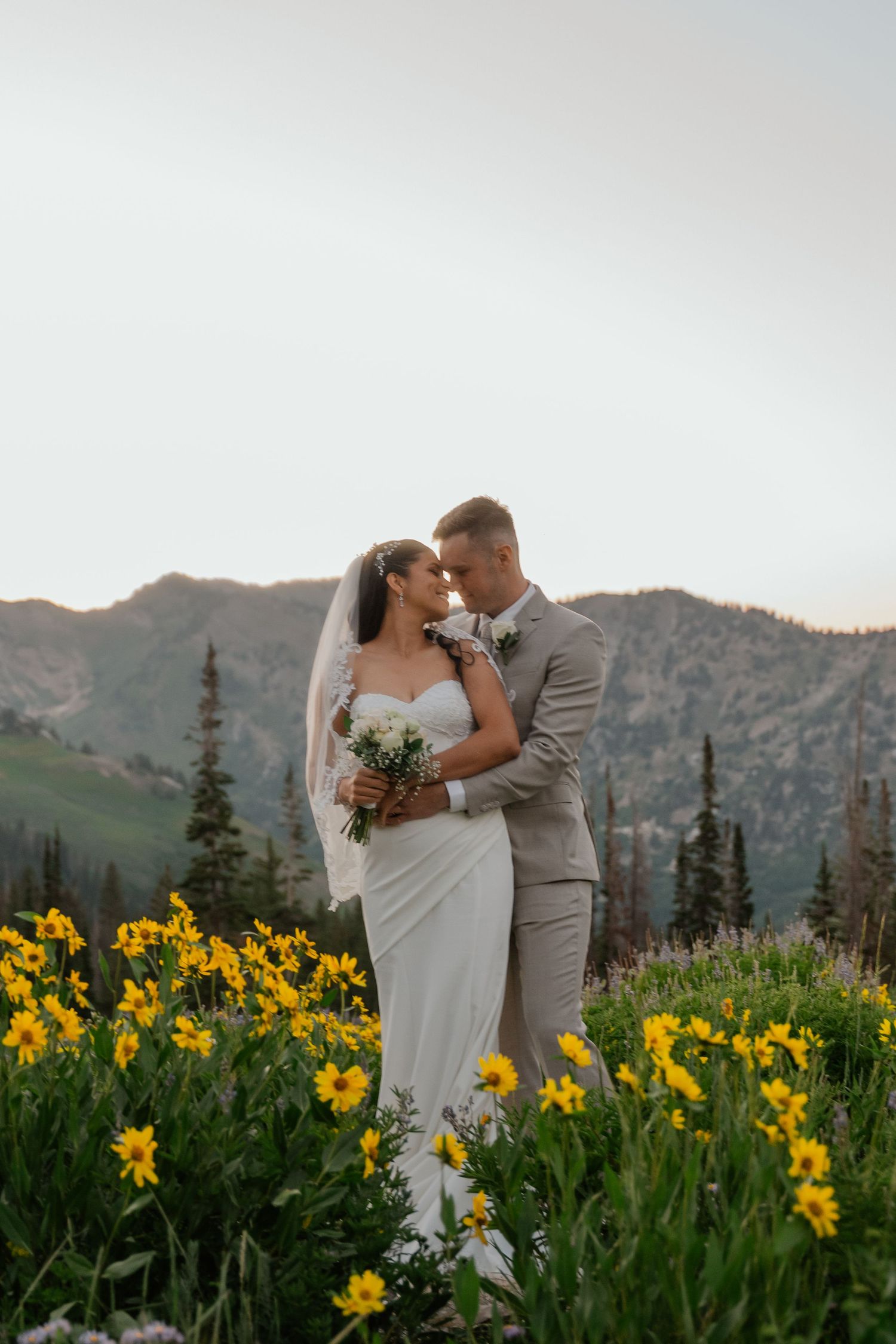 Bride and groom share romantic moment in wildflower meadow at sunset.