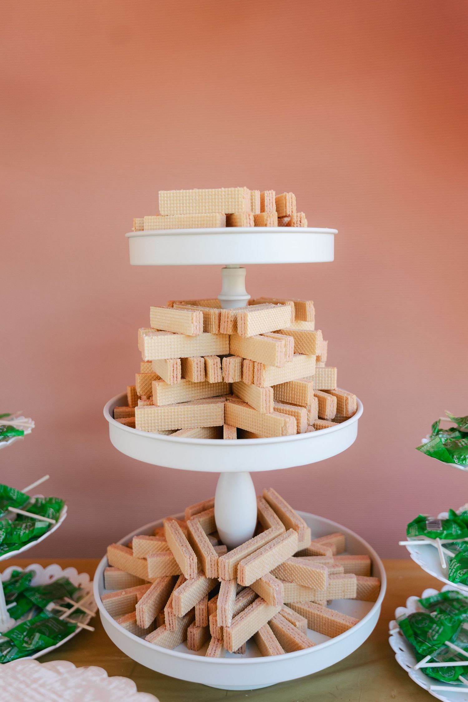 Three-tier white cake stand displaying stacked wafer cookies and biscuits at a dessert table.