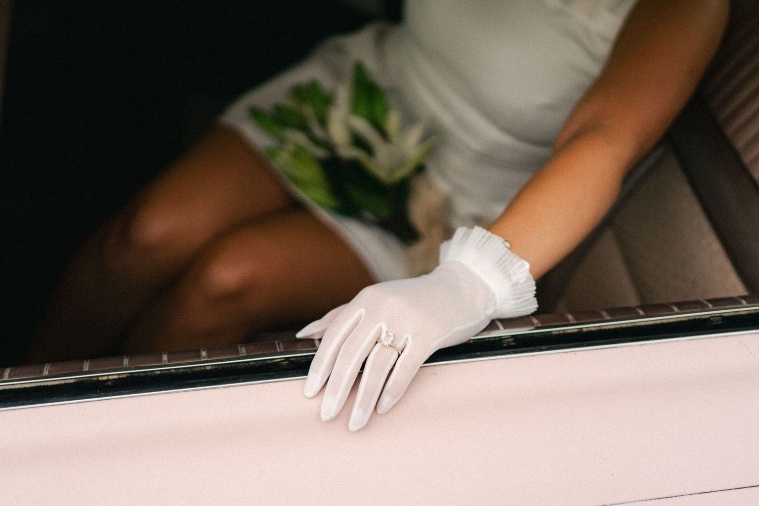 Bride in white gloves resting hand on car window in elegant wedding detail photo.