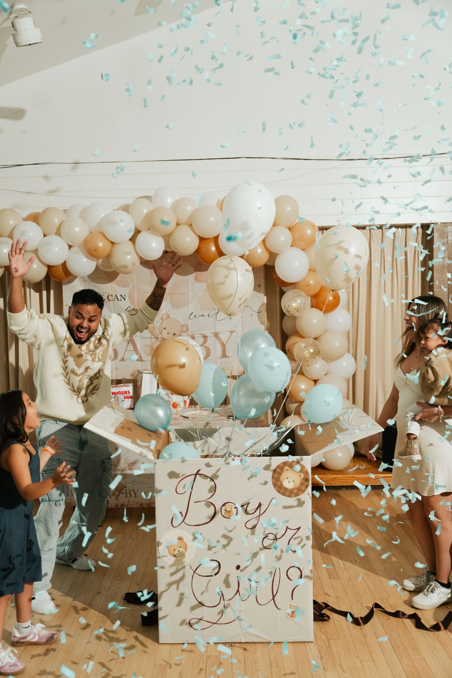 Gender reveal party with blue confetti explosion and Boy or Girl sign surrounded by balloons.
