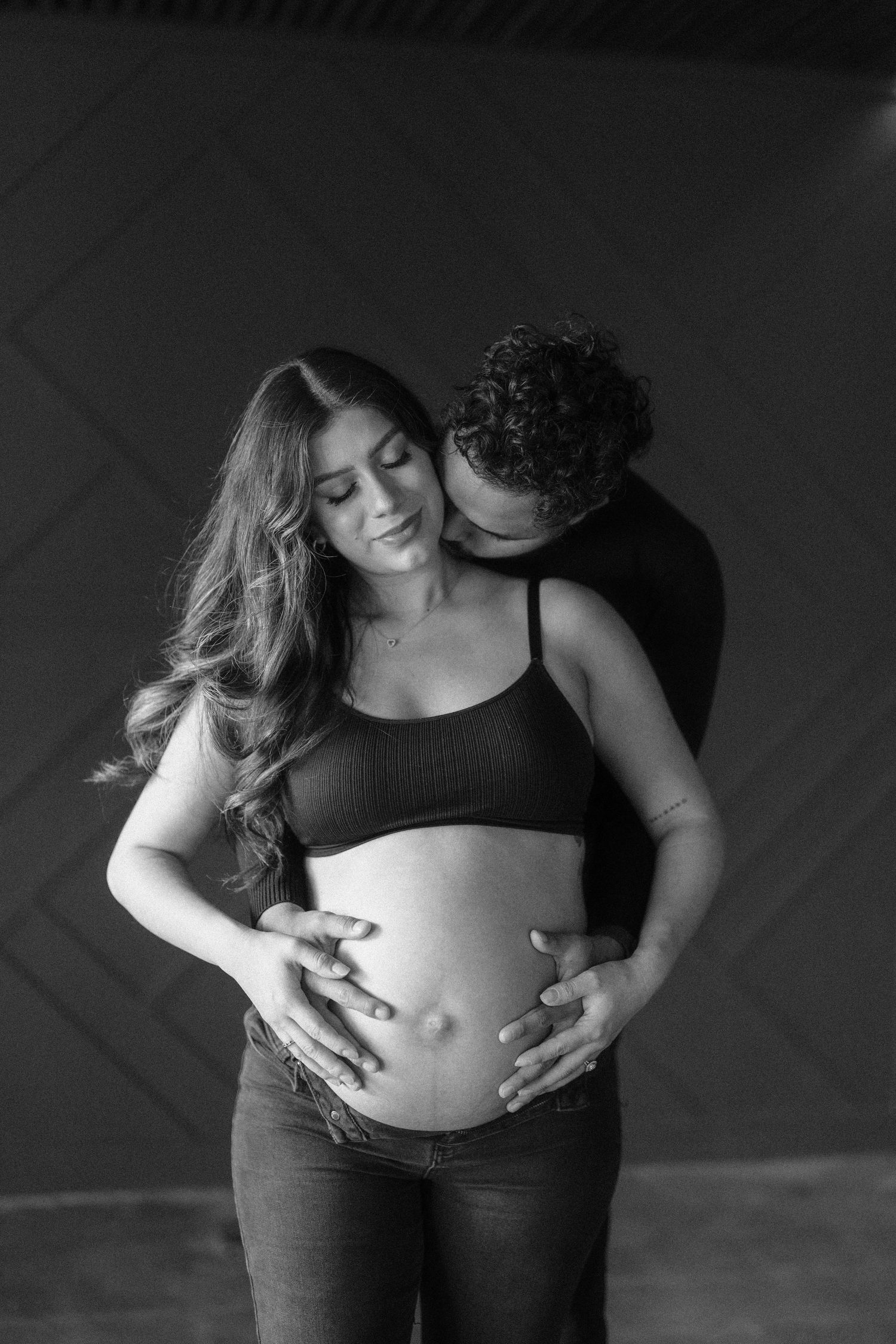 Black and white maternity photo of couple embracing and cradling pregnant belly tenderly.