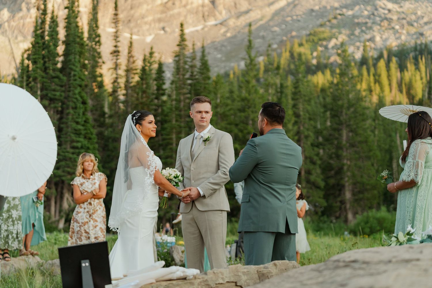 Couple exchanges vows outdoors with mountain backdrop and pine trees.