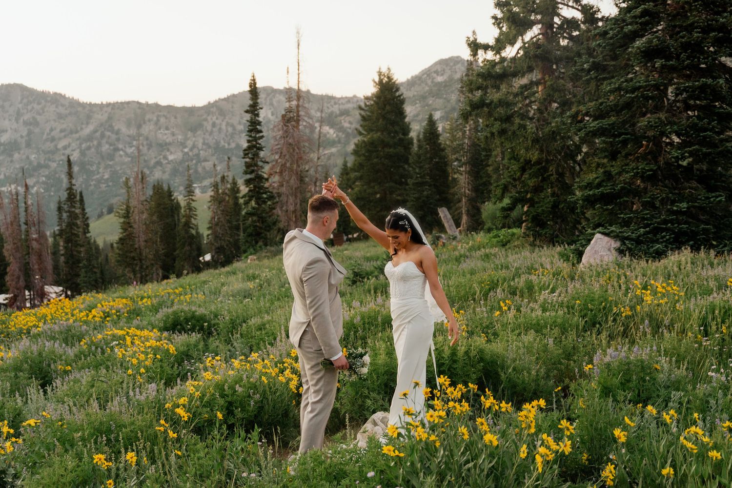 Bride and groom dancing in a wildflower meadow with mountain and pine tree backdrop during outdoor wedding.