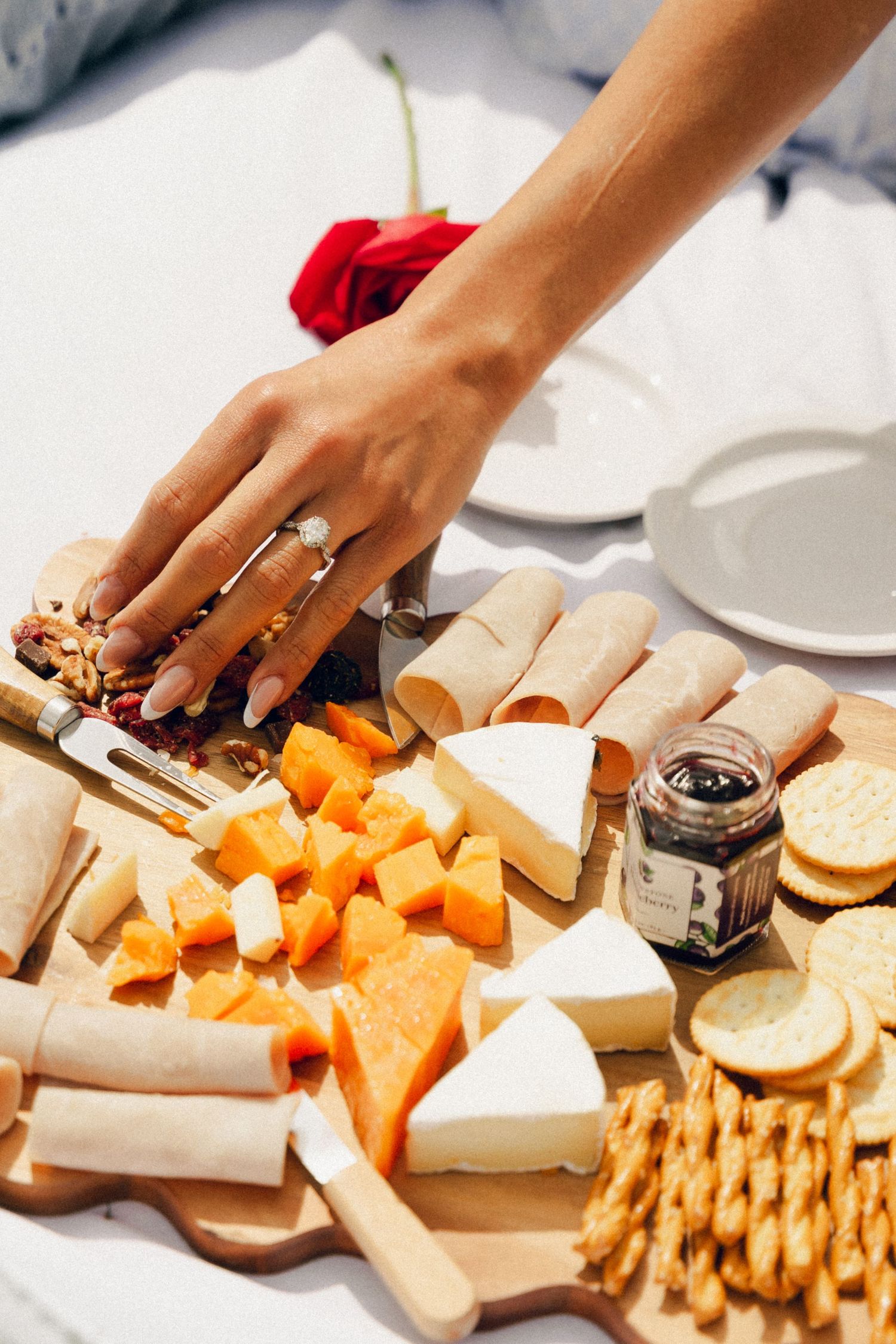 A hand with rings reaches for a charcuterie board with cheese, crackers, and fruit.