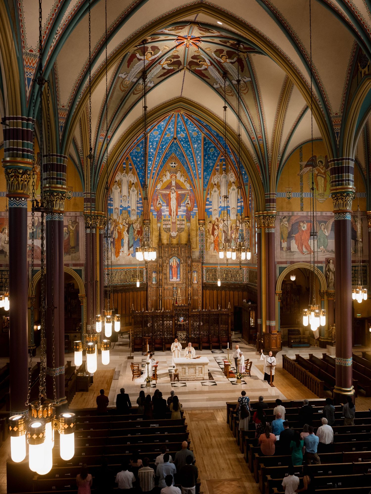 Ornate Gothic cathedral interior with colorful murals, vaulted ceilings, and congregation gathered for a religious ceremony.