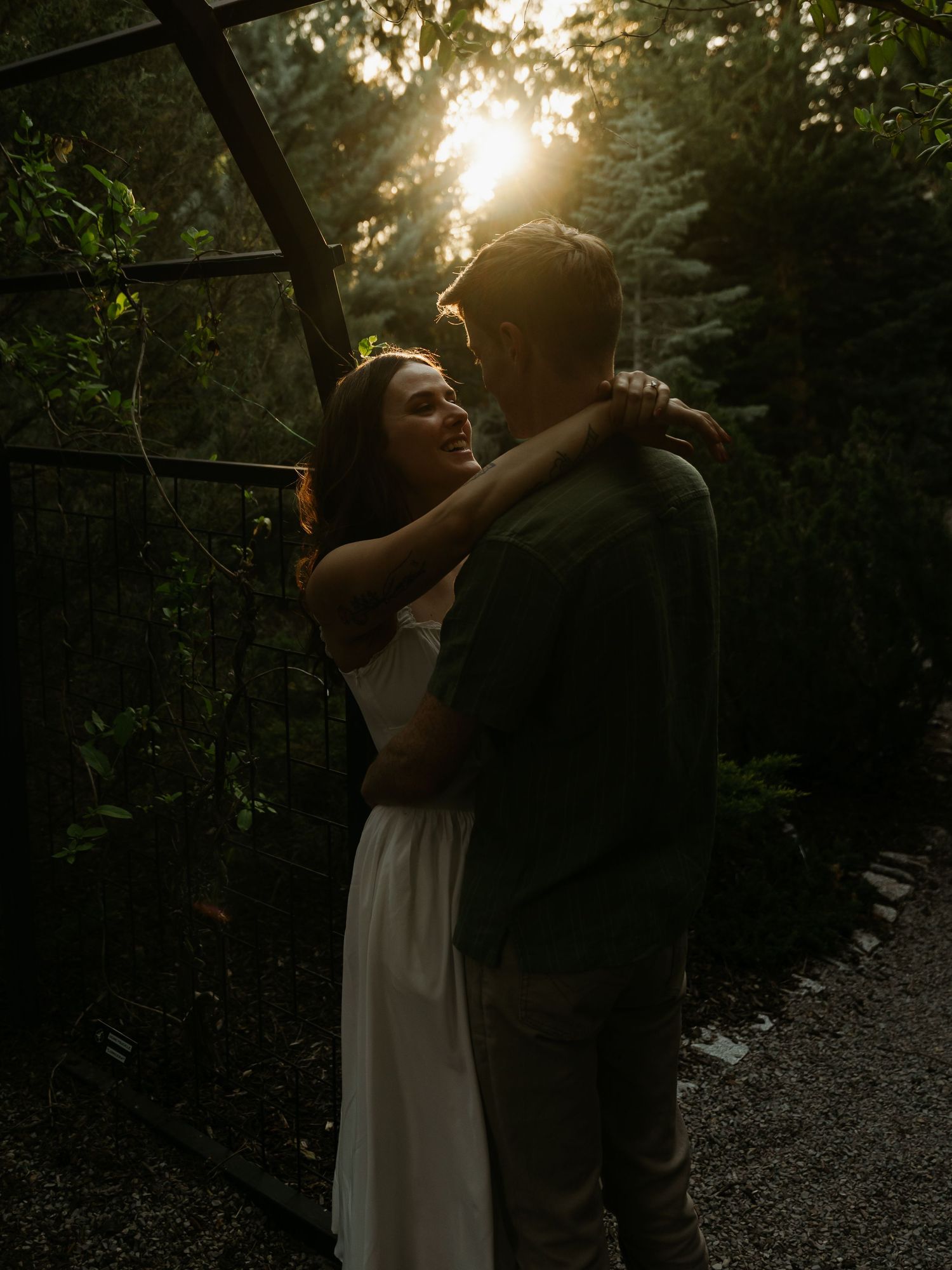 Couple embracing at sunset in a lush garden, golden backlight creating a romantic and dreamy atmosphere.
