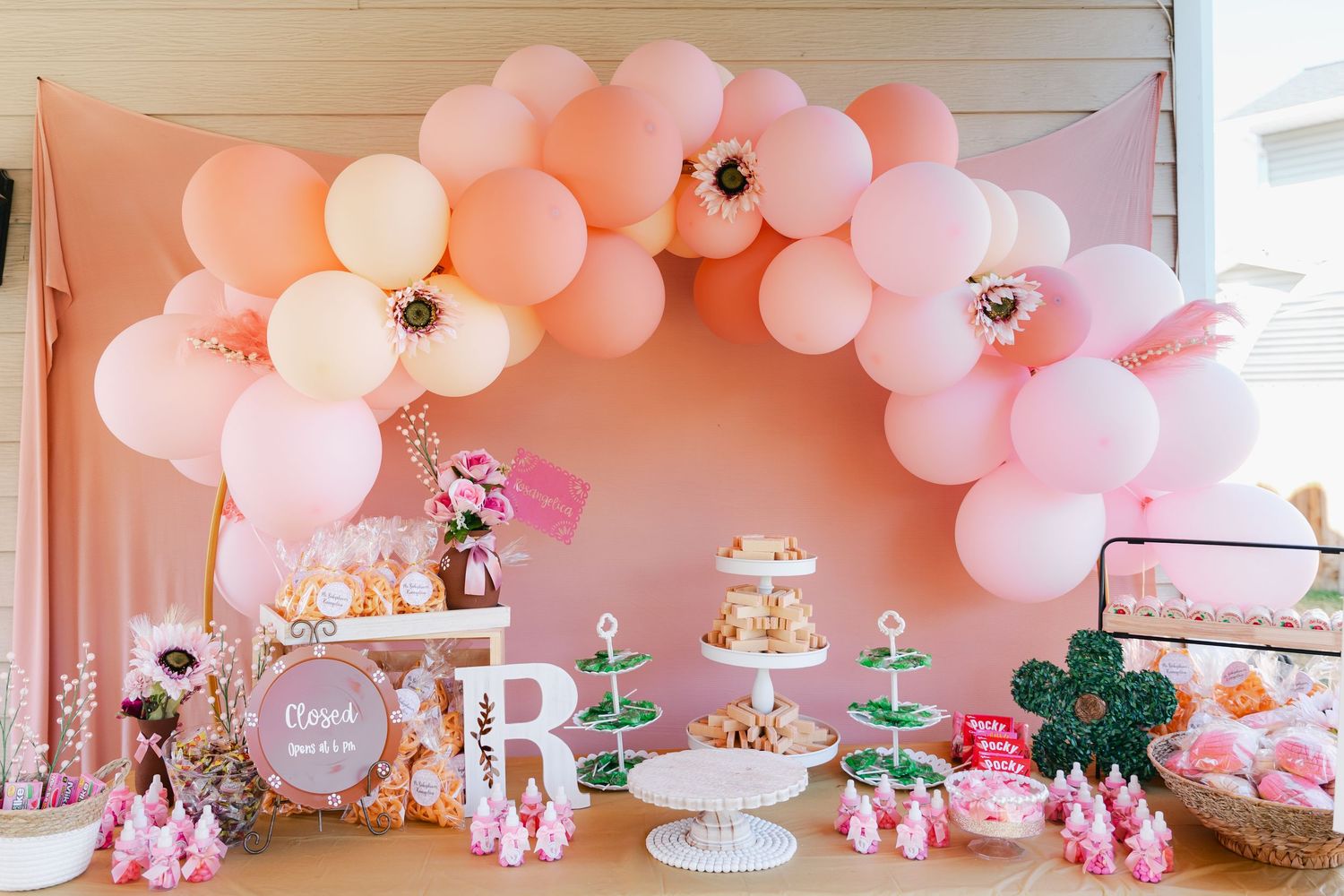 Pink balloon arch over dessert table with tiered cake and treats at elegant baby shower.