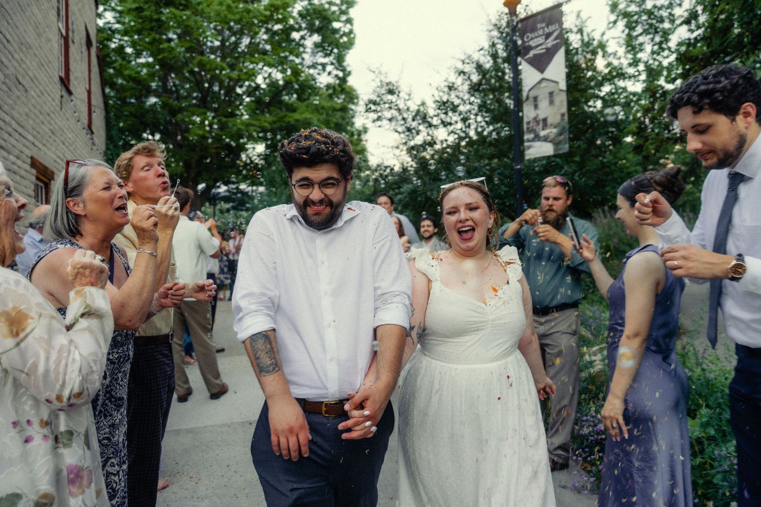 Happy couple walks hand-in-hand at outdoor wedding celebration surrounded by cheering guests.