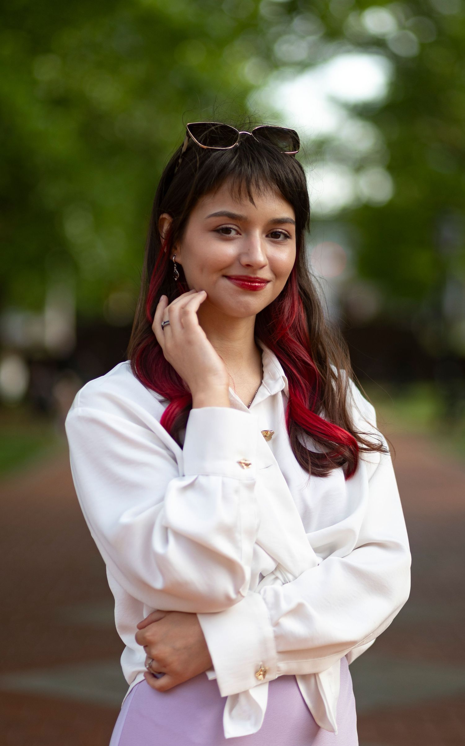 A stylish, natural light portrait of a smiling woman posing outdoors on a campus walkway, captured by a professional portrait photographer.