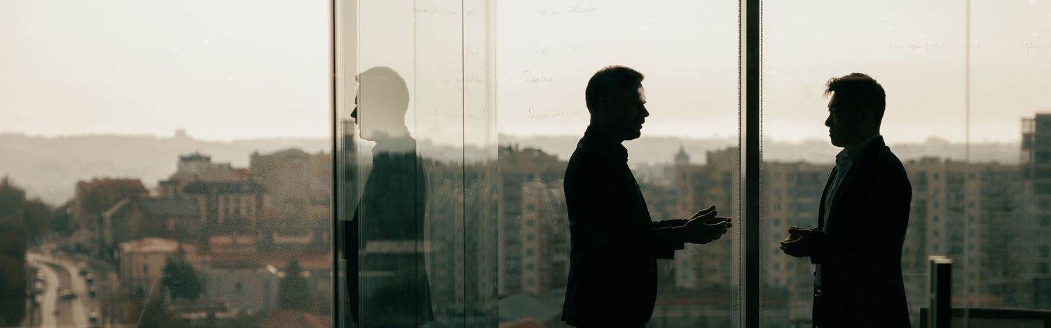 A cinematic silhouette portrait of two professionals standing by a window overlooking a city skyline.