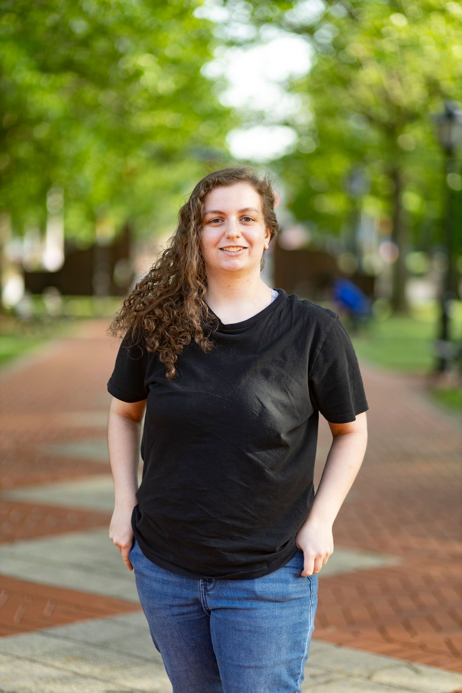 A casual natural light portrait of a smiling woman outdoors on a campus path, captured by a professional portrait photographer.