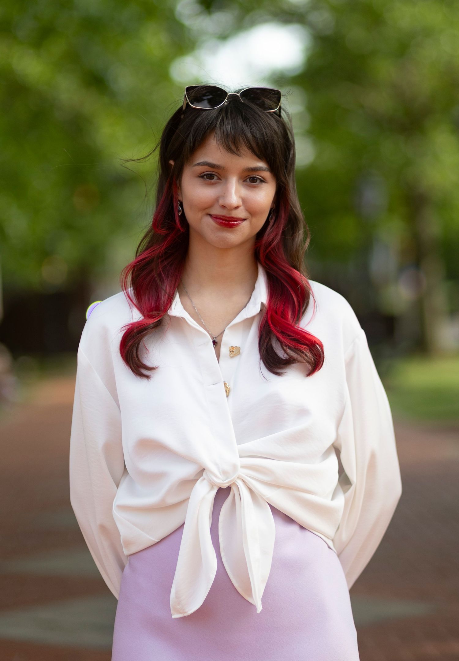 A centered, natural light portrait of a stylish woman smiling outdoors on a brick path, captured by a professional portrait photographer.