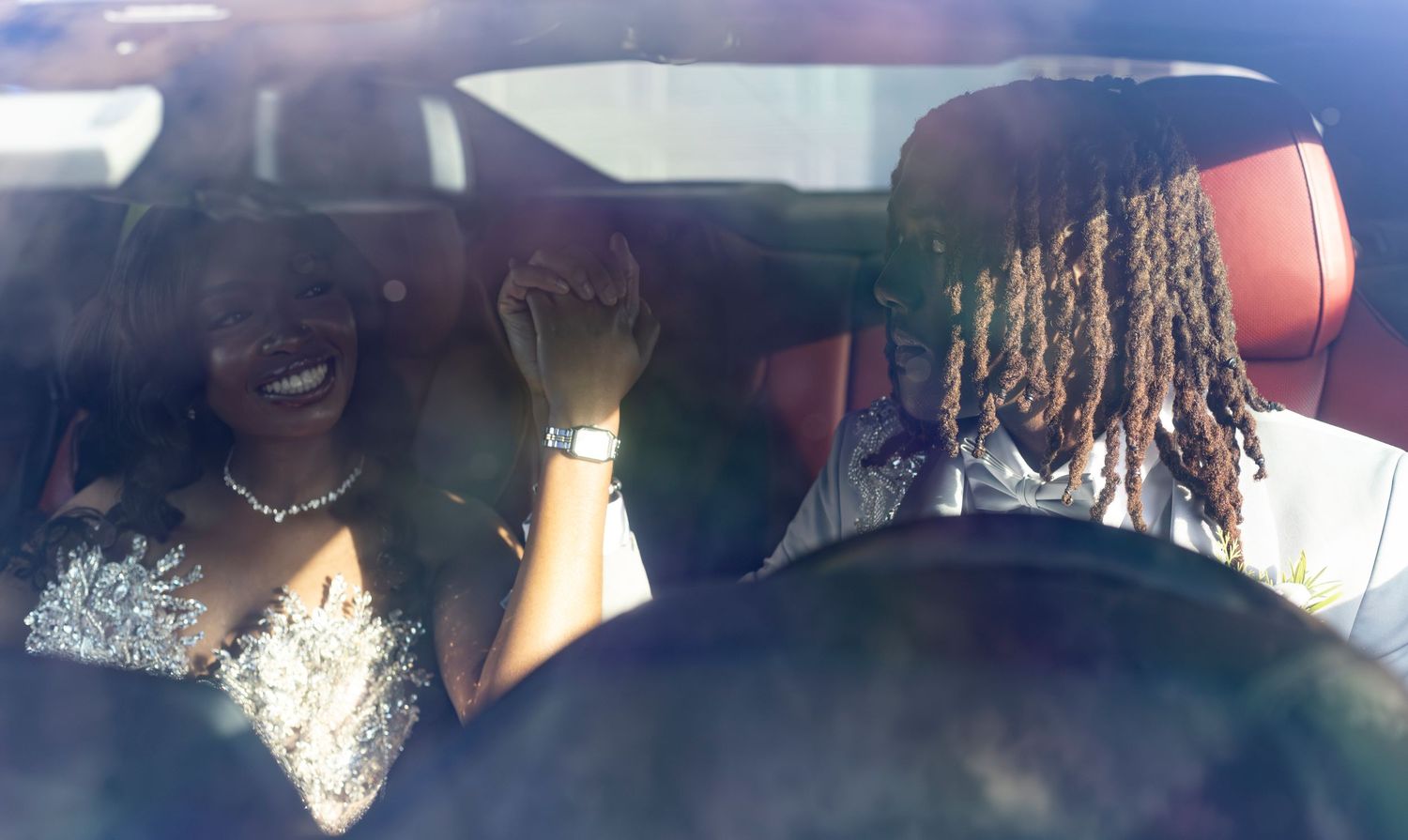 Young couple holding hands in formal prom wear, viewed through a car windshield during a milestone photography shoot.