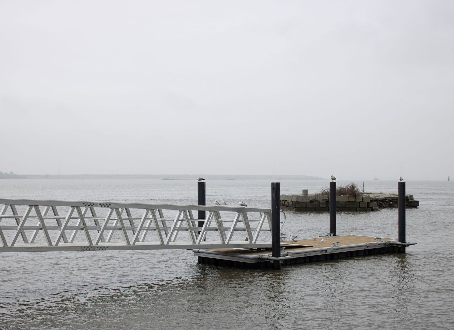 A metal gangway leading to a floating dock on quiet open water under an overcast sky, captured by a professional landscape photographer.