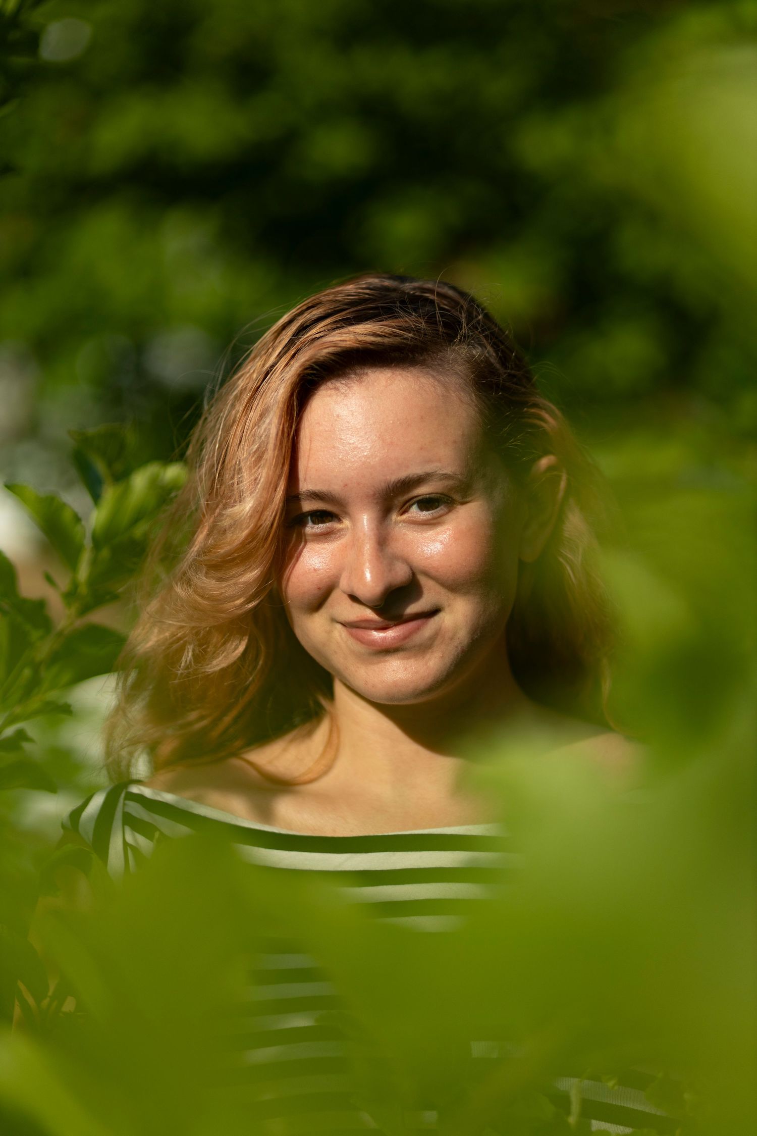 A natural light portrait of a smiling woman framed by vibrant green foliage, perfect for an outdoor portrait and headshot photography.