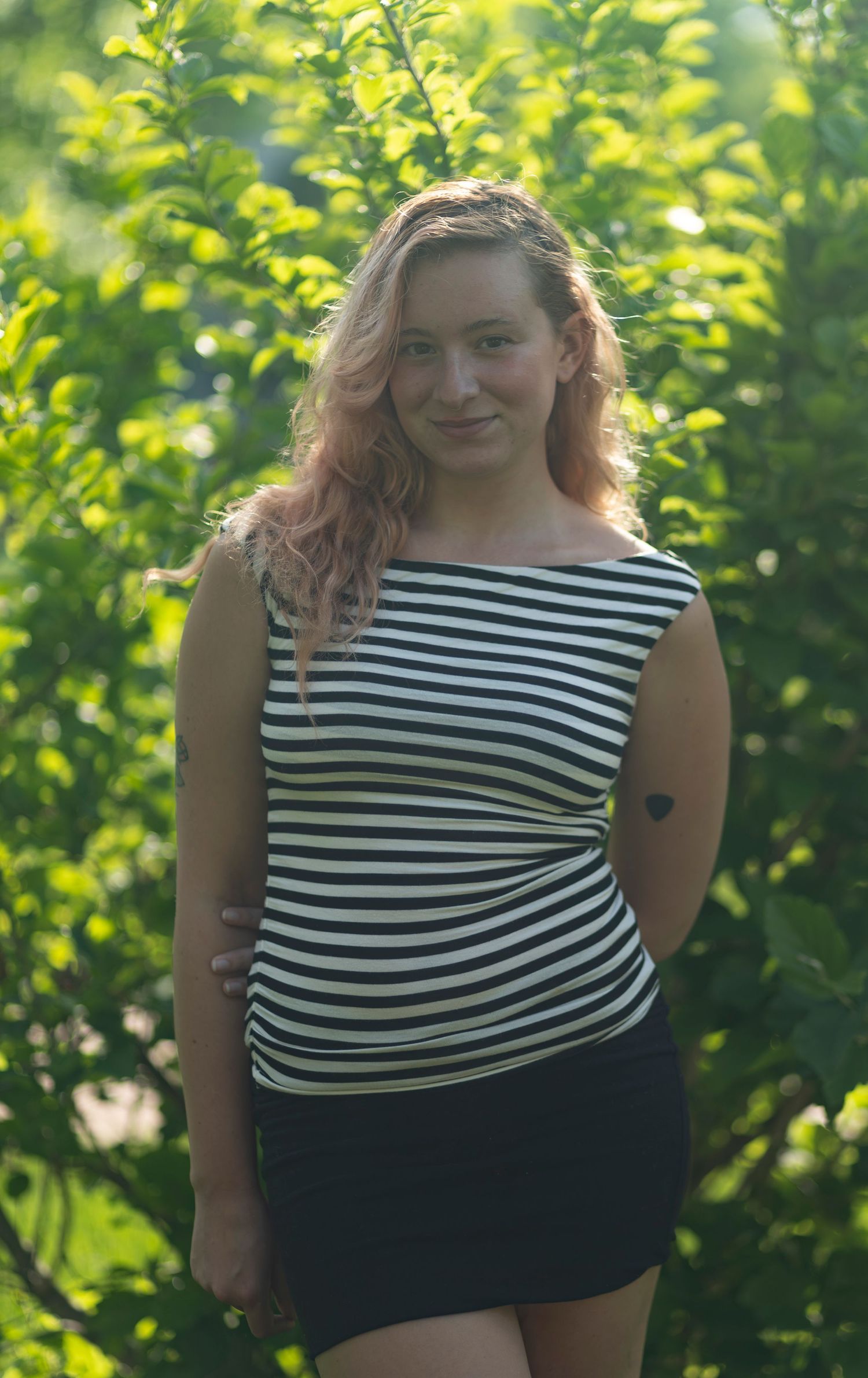A backlit outdoor portrait of a smiling woman in a striped shirt, captured by a professional portrait photographer.