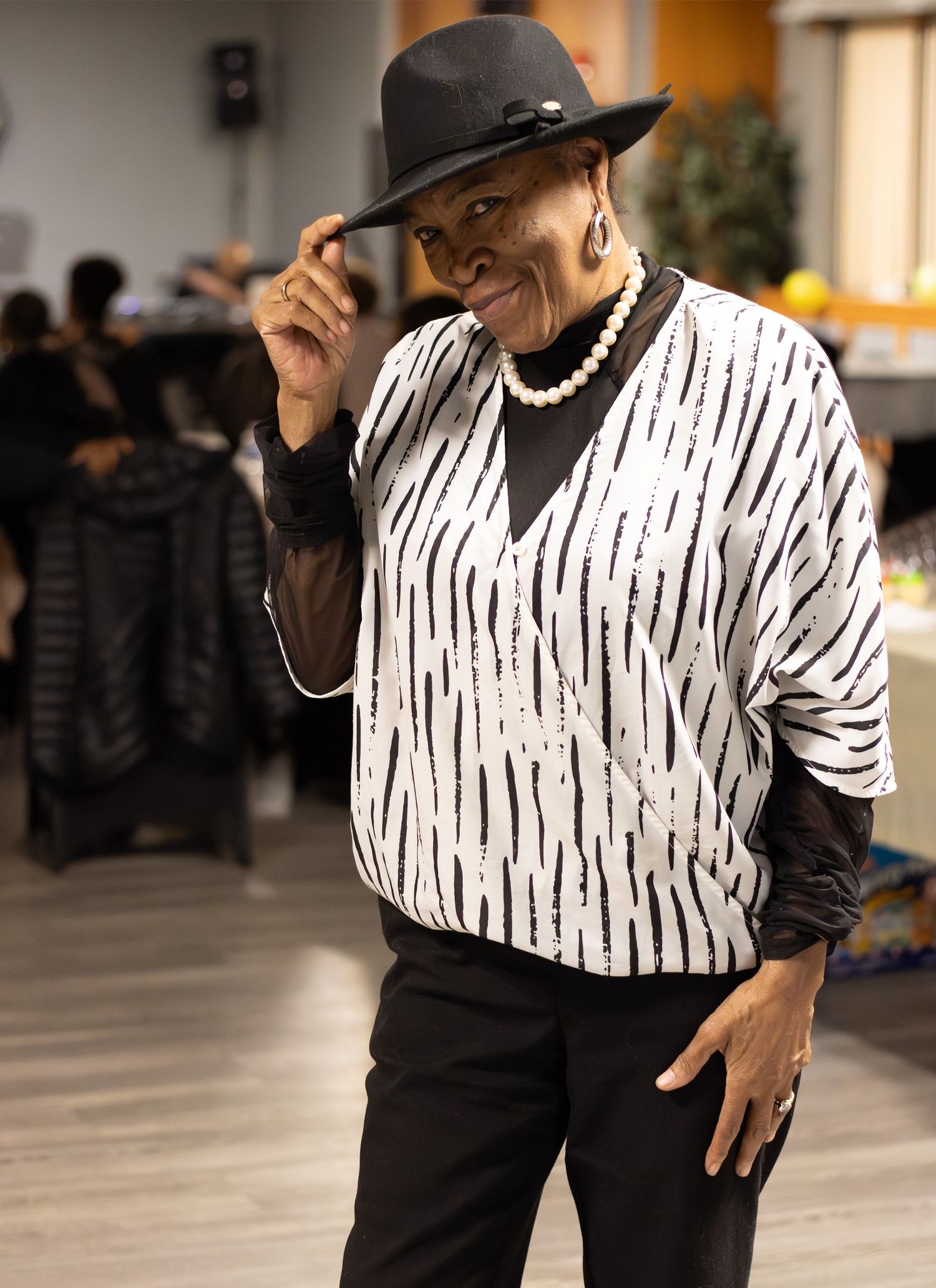 A joyful portrait of an elegant woman in a hat posing at an indoor event, captured by a professional photographer.