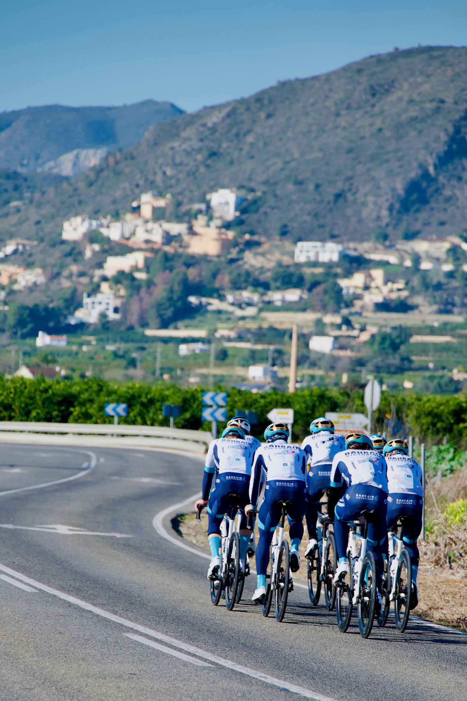 Team Bahrain Victorious cycling team during a 2025 training camp near Pego, in Spain, with a mountainous backdrop.