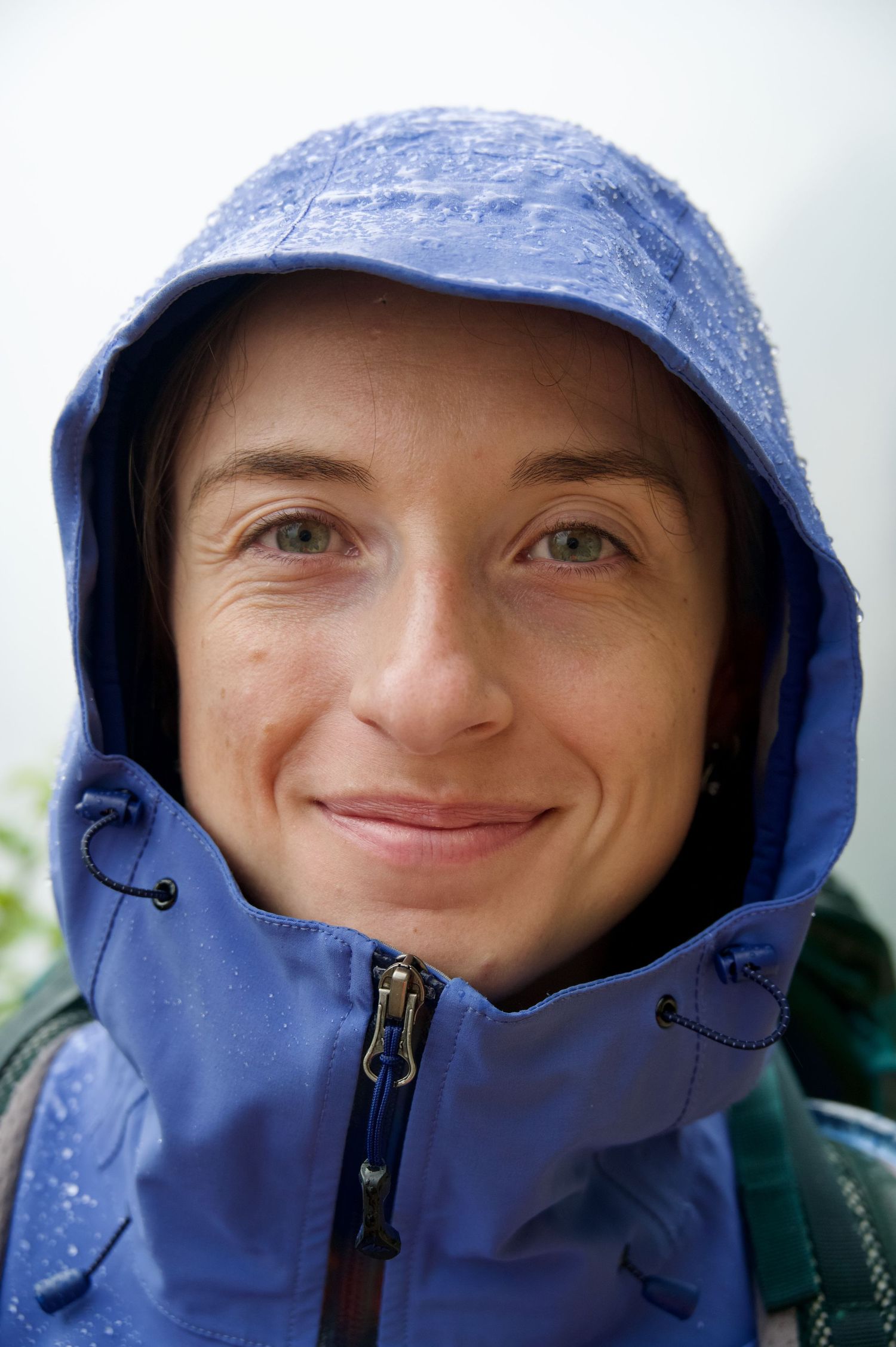 Close up of a woman's face whilst she is wearing a blue waterproof with water drops.