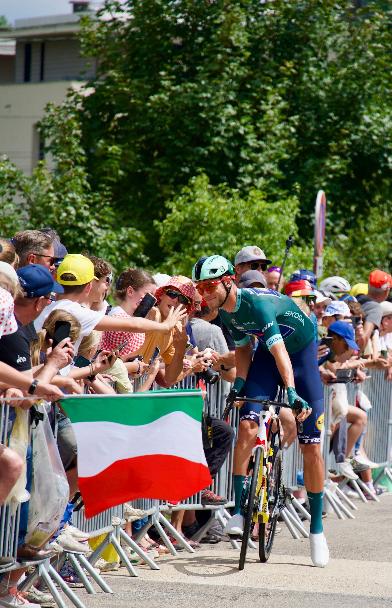 Jonathan Milan posing for a photograph with fans at the start of the 18th Stage of the 2025 Tour de France in front of an Italian flag.