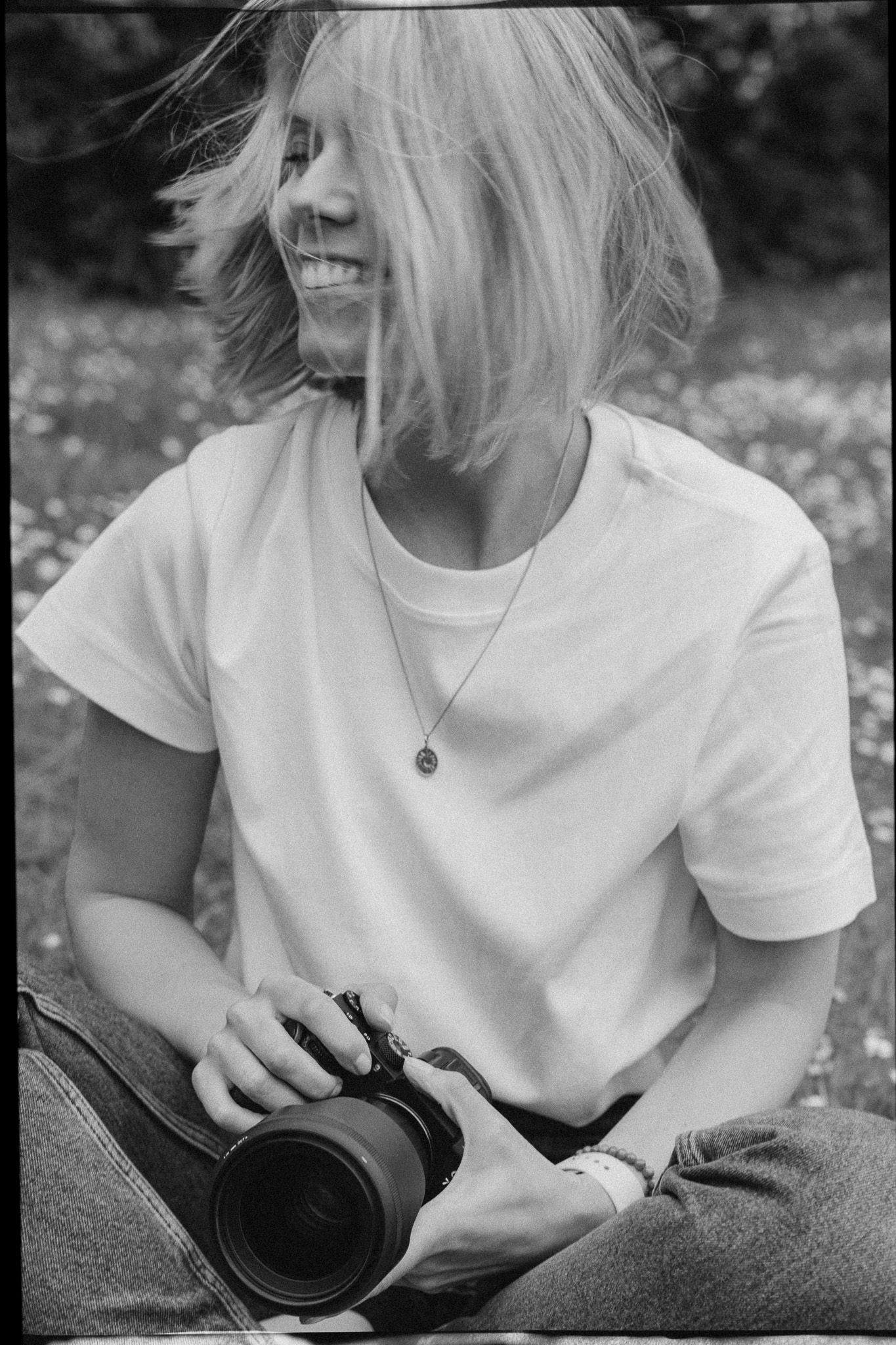 Candid black and white photo of photographer holding camera while sitting in flower field.