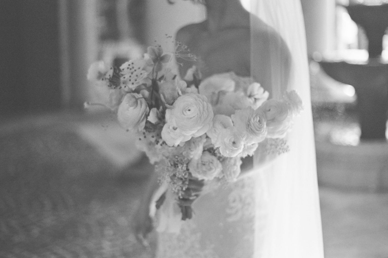 A delicate bouquet of white roses and flowers tied with ribbon in soft black and white focus.