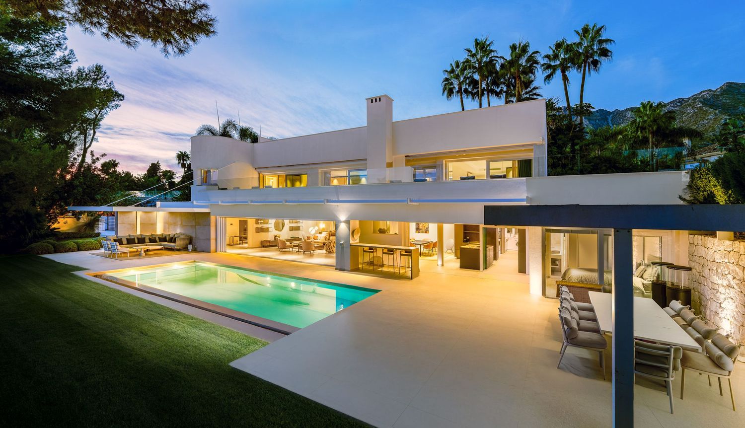 Luxury villa photographed at dusk in Málaga, with warm interior lighting and soft evening tones highlighting architecture and outdoor spaces