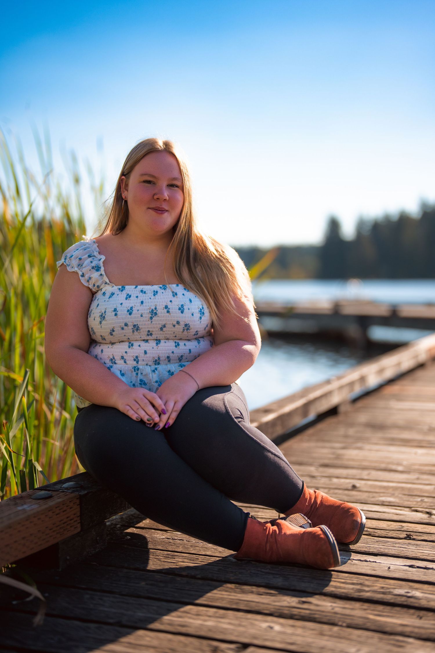 Person sitting on wooden dock by lake during golden hour.