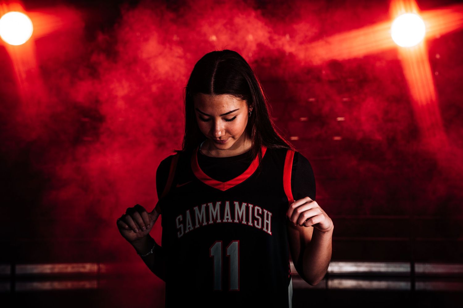 Athlete in dark uniform posing with dramatic red lighting and smoke effects.