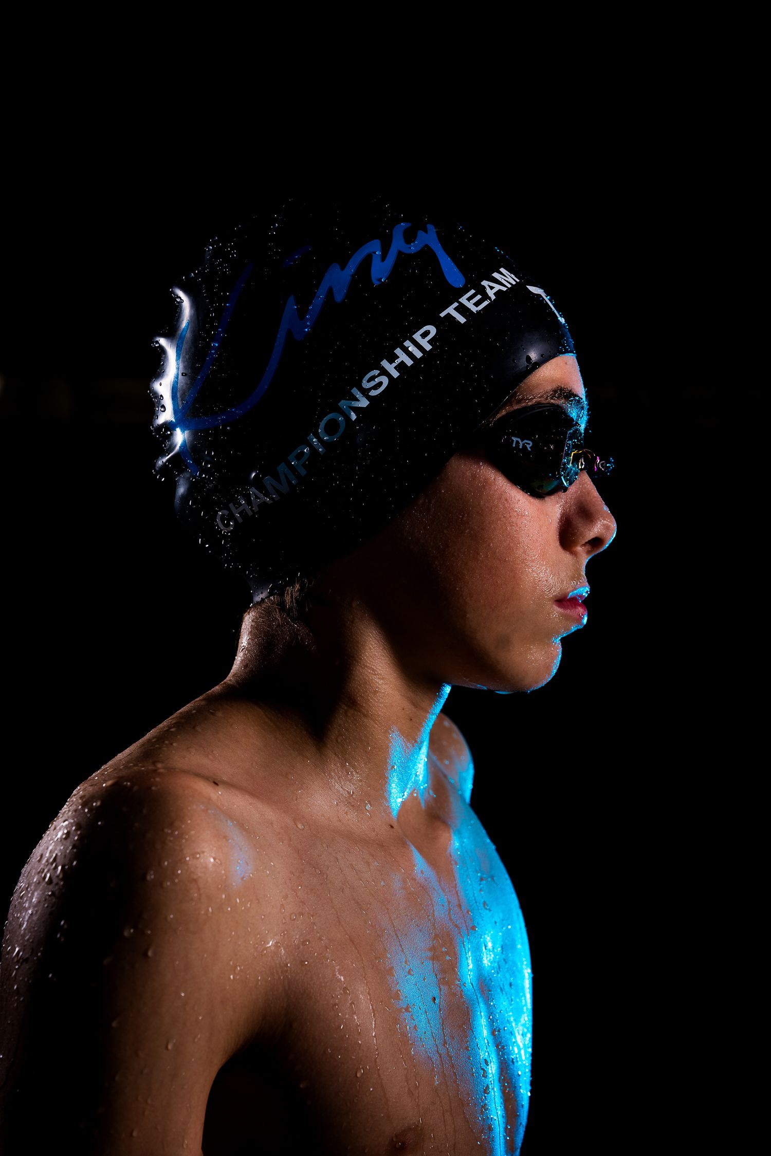 Swim team members in blue caps photographed in dramatic side profile against dark background.