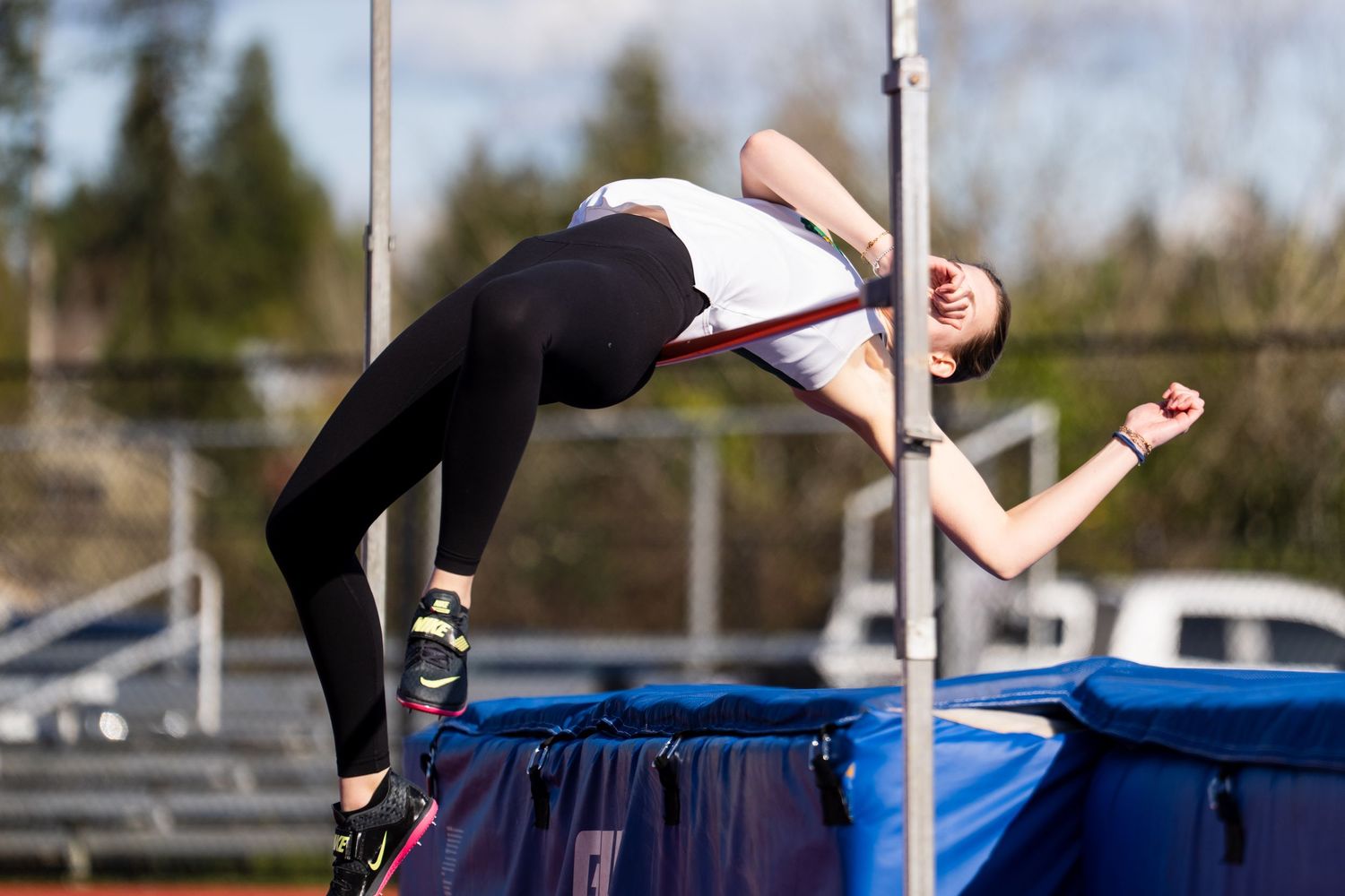 High school athlete clearing the bar during track and field high jump competition with blue landing mat below.