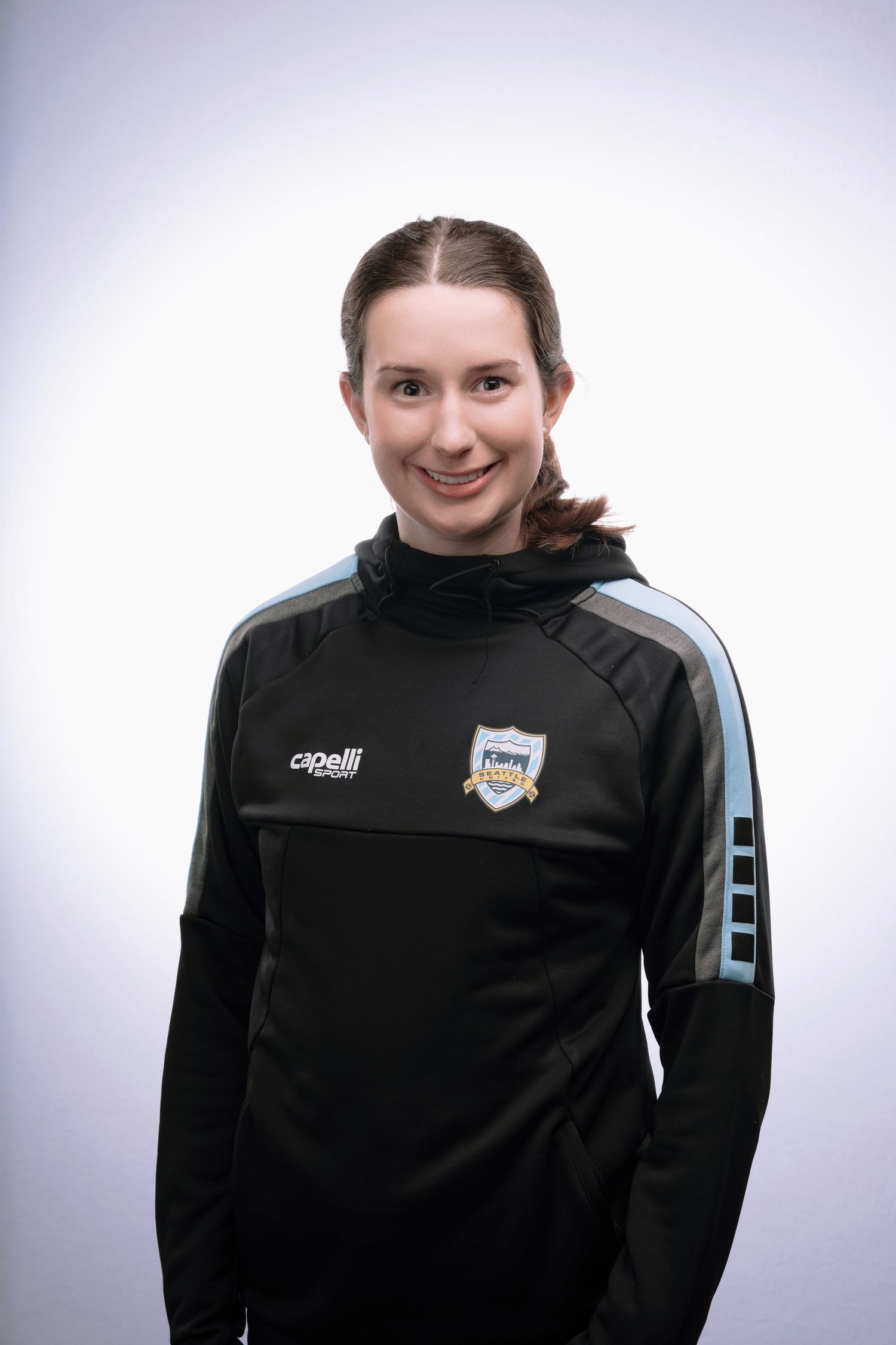 Four headshots showing someone wearing a black athletic jacket with a team logo against a light background.