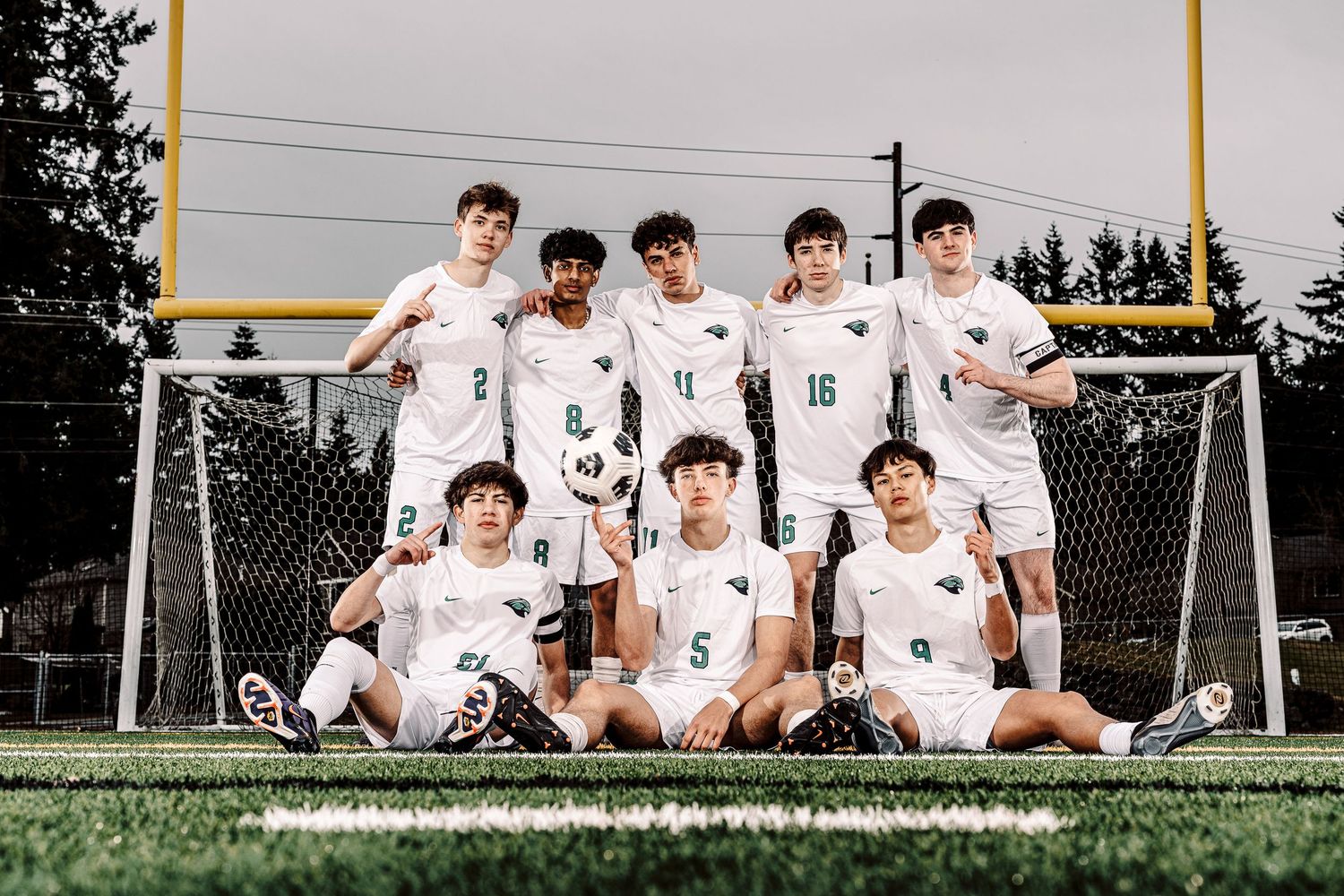 Soccer team players in white uniforms pose together on field during team photo session.