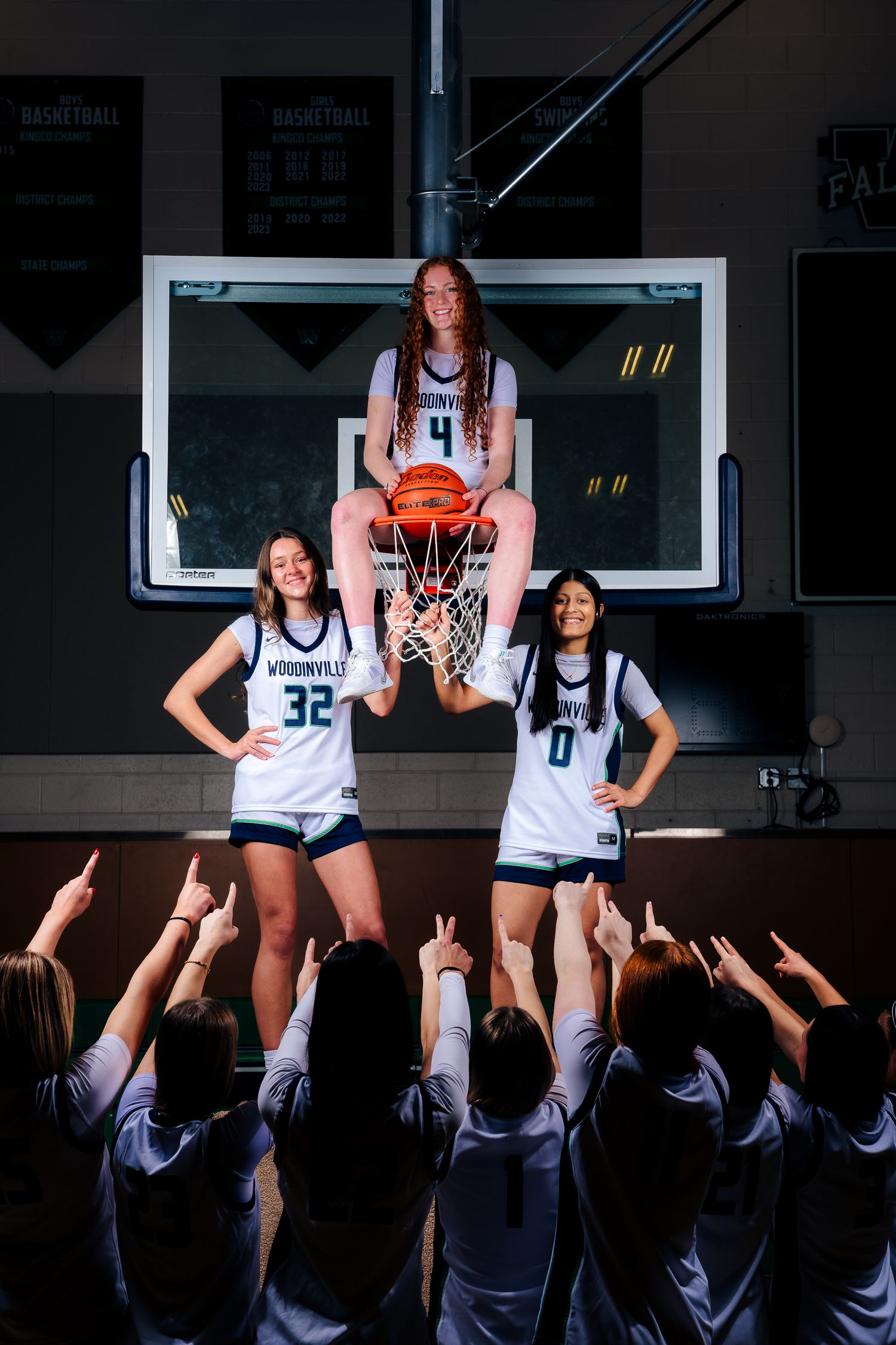Basketball players in white jerseys pose on elevated platforms while teammates reach up from below in dramatic lighting.