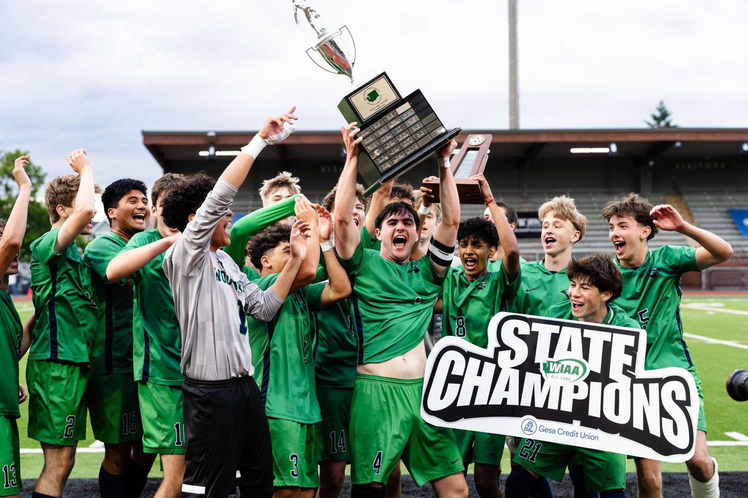 High school sports team celebrates with trophy and state championship banner.