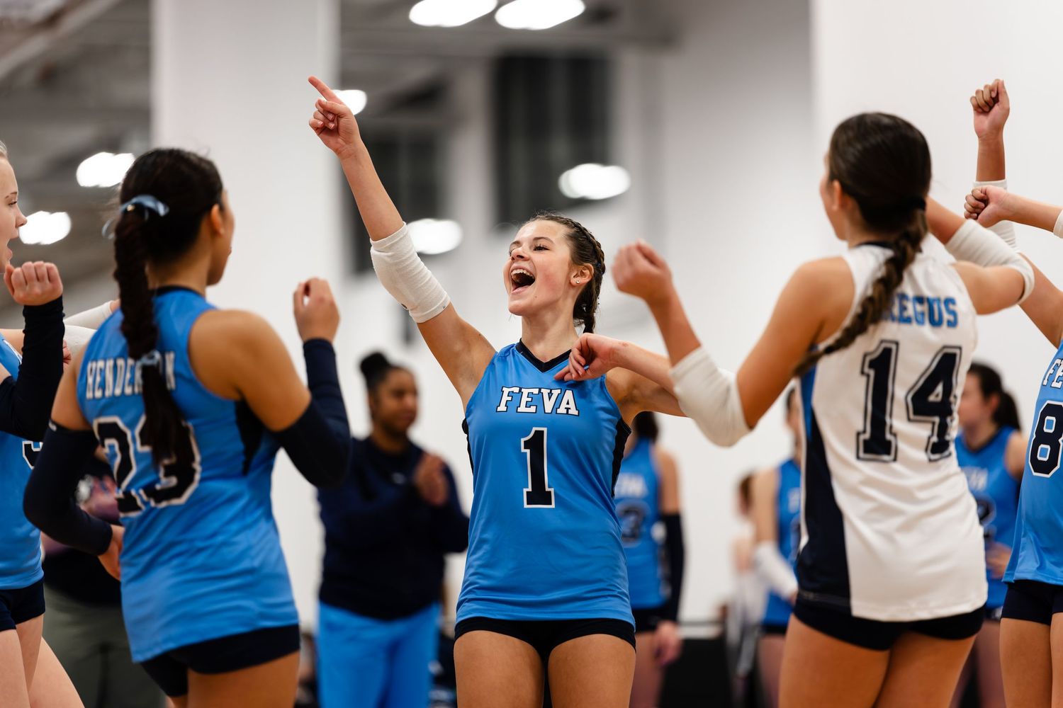 Volleyball players in blue and white jerseys celebrate together with raised arms during an intense match.