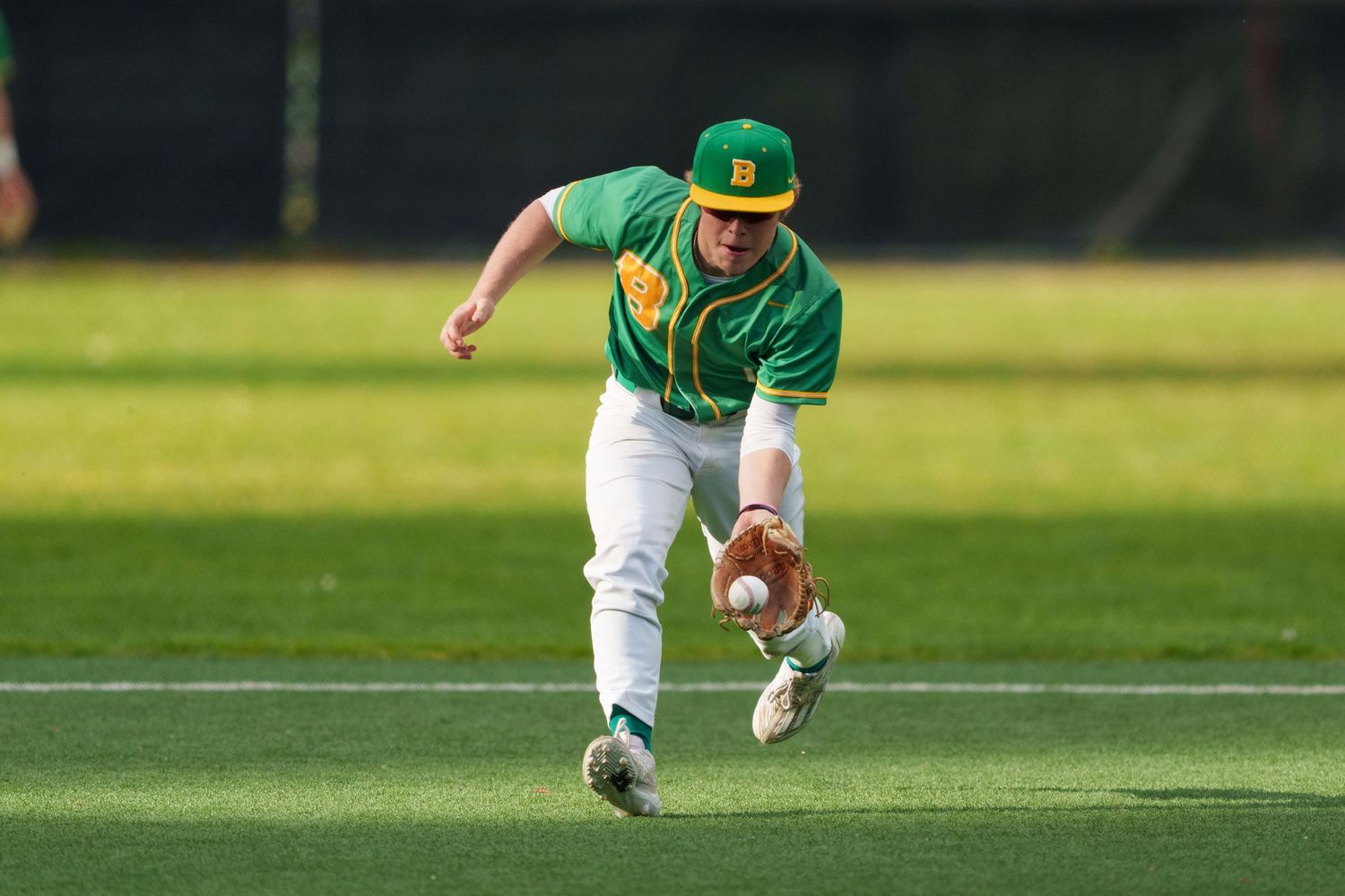 Baseball player in green and white uniform dives to catch a ball during a game.