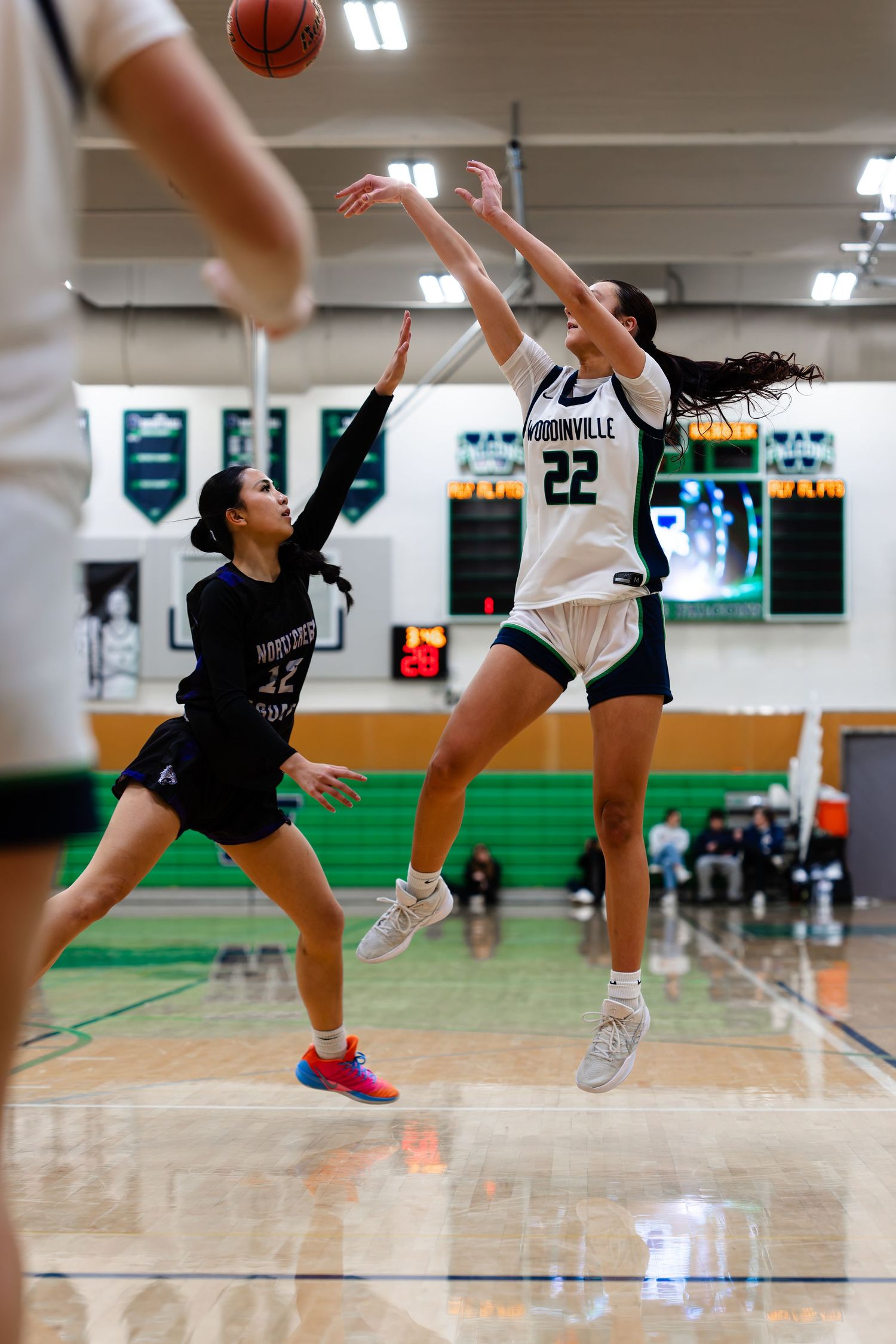 Basketball players compete for a loose ball during an intense indoor game on a green-lit court.