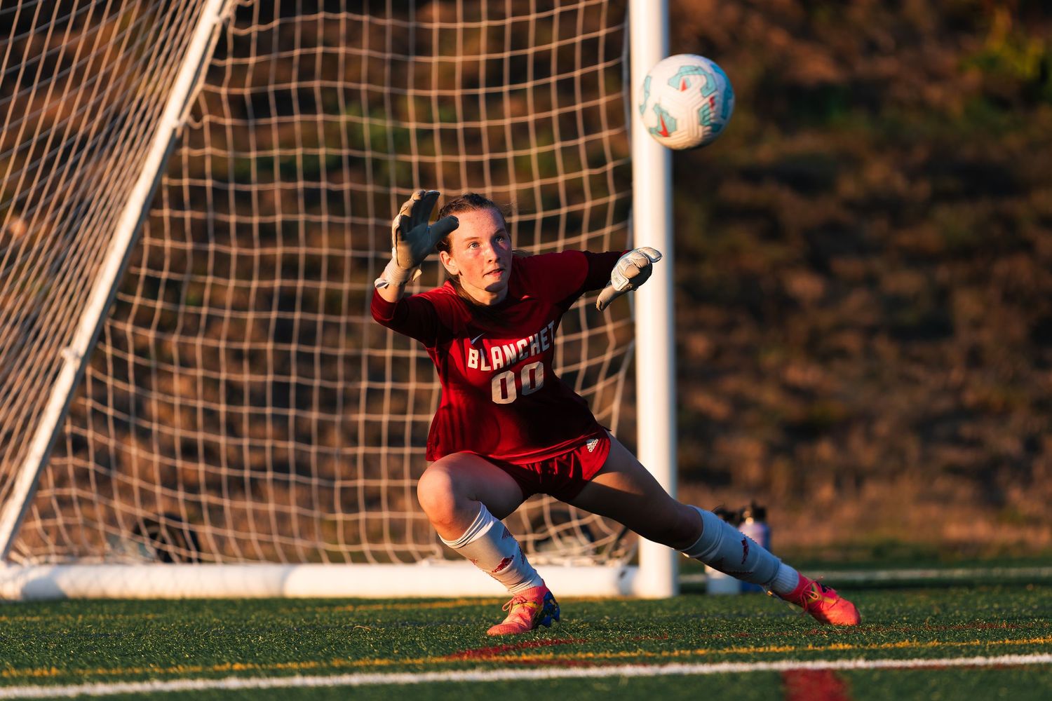 Soccer goalkeeper in red uniform makes a diving save attempt to block the ball during a match.