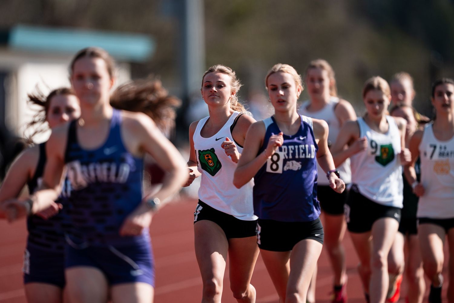 Track and field athletes compete in a distance running race on an outdoor track during a competition.
