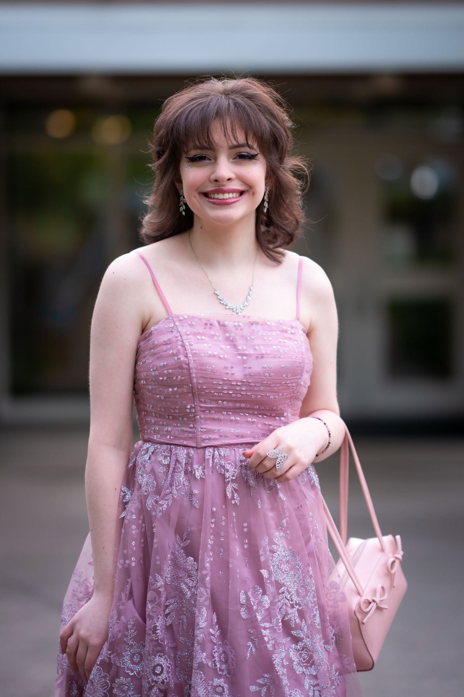 Portrait of someone wearing a pink sparkly formal dress with matching purse outdoors.