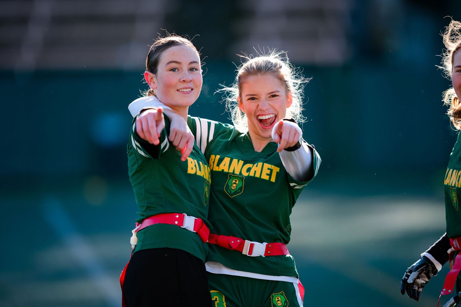 Youth athletes in green uniforms celebrate together outdoors during a sports event.
