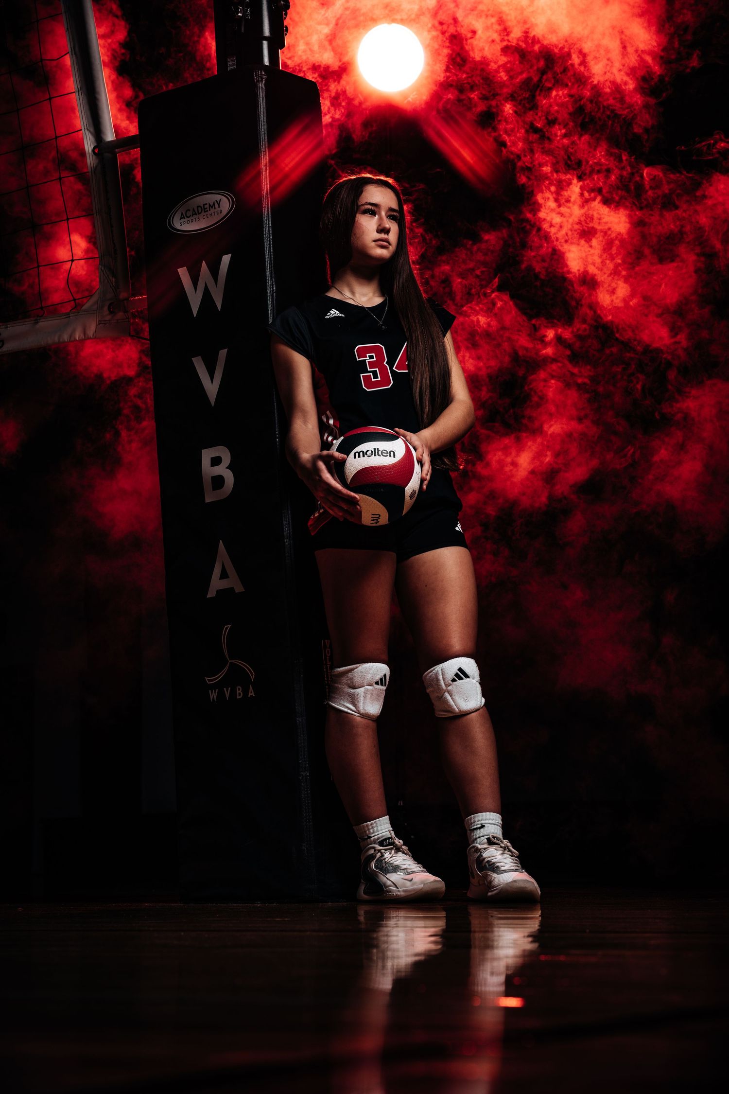 Volleyball players posing in black uniforms with dramatic red smoke effects on dark court.