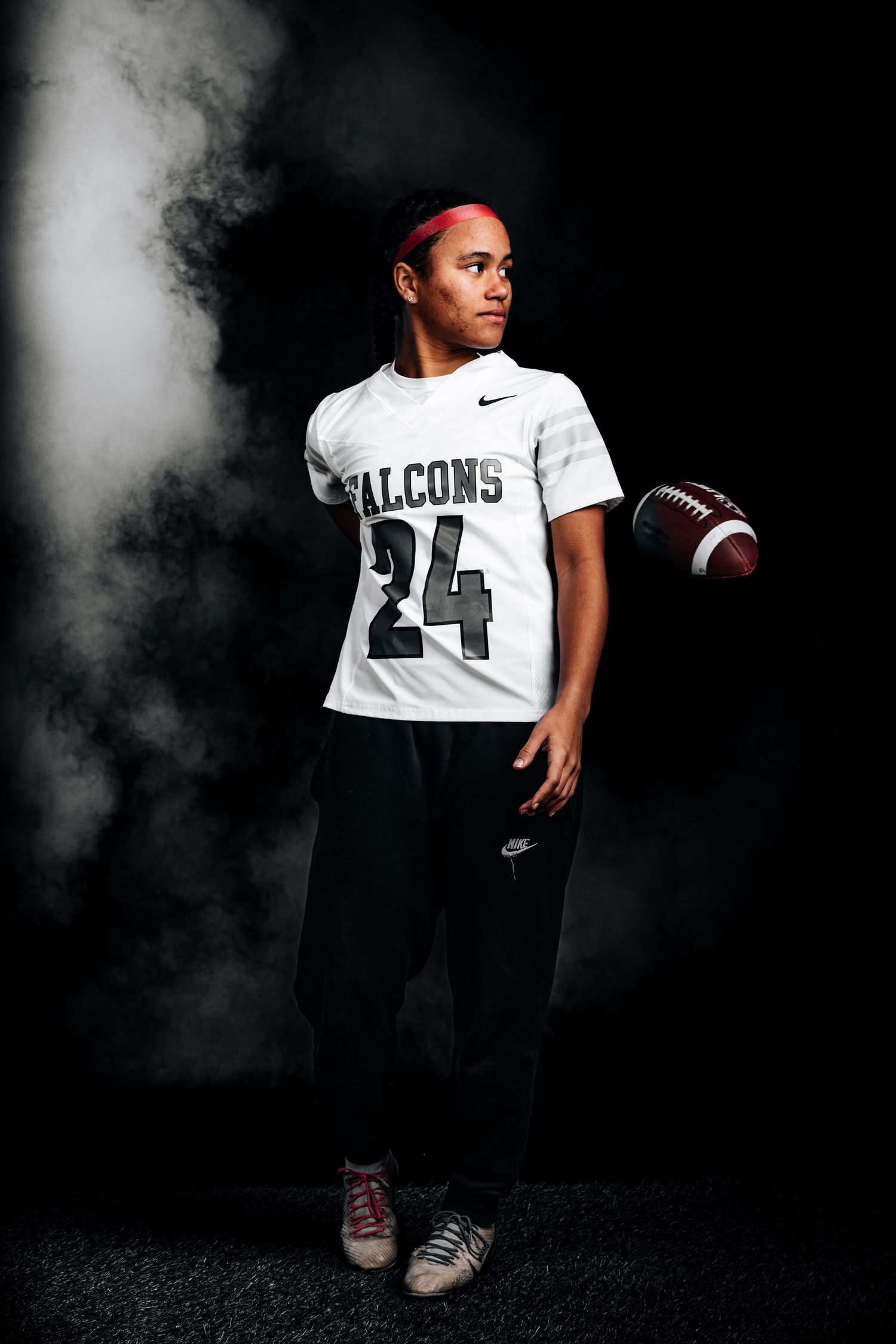 Athlete in Falcons jersey number 24 poses with football against dark background with dramatic smoke effect.
