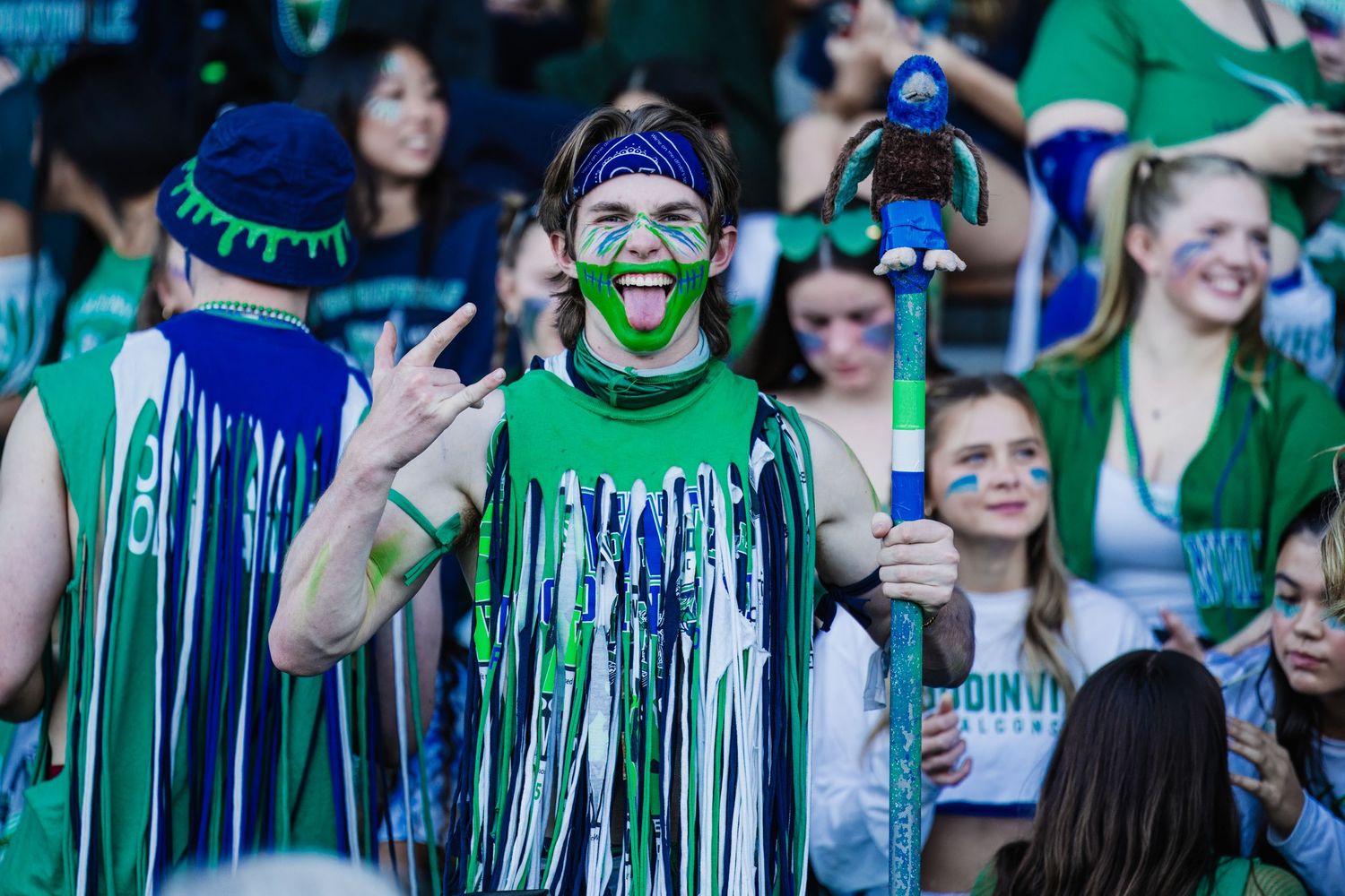 Enthusiastic sports fan in green and blue face paint and matching streamers cheers excitedly at a game.