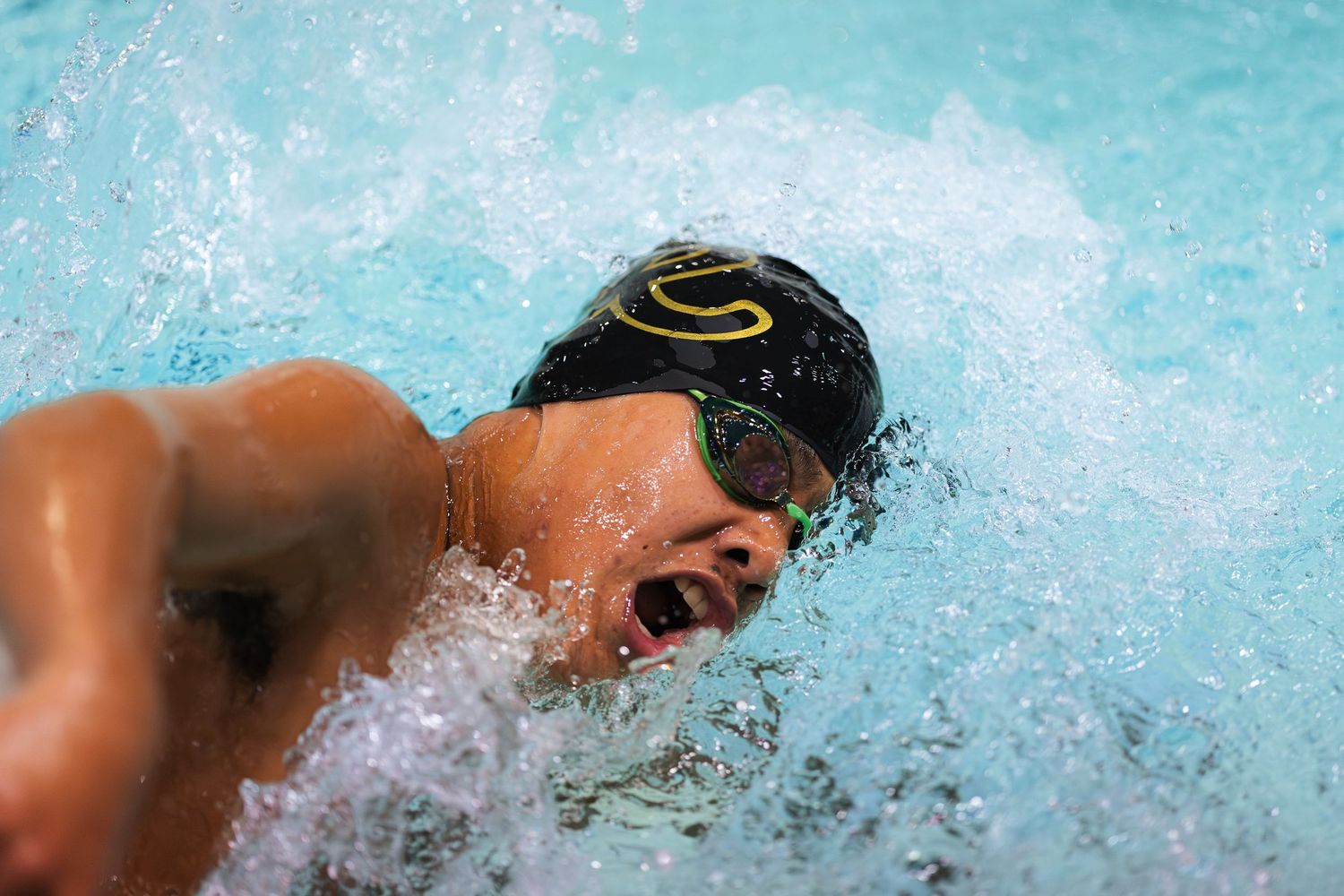 A swimmer in a black cap emerges from the water while competing in a swimming race.