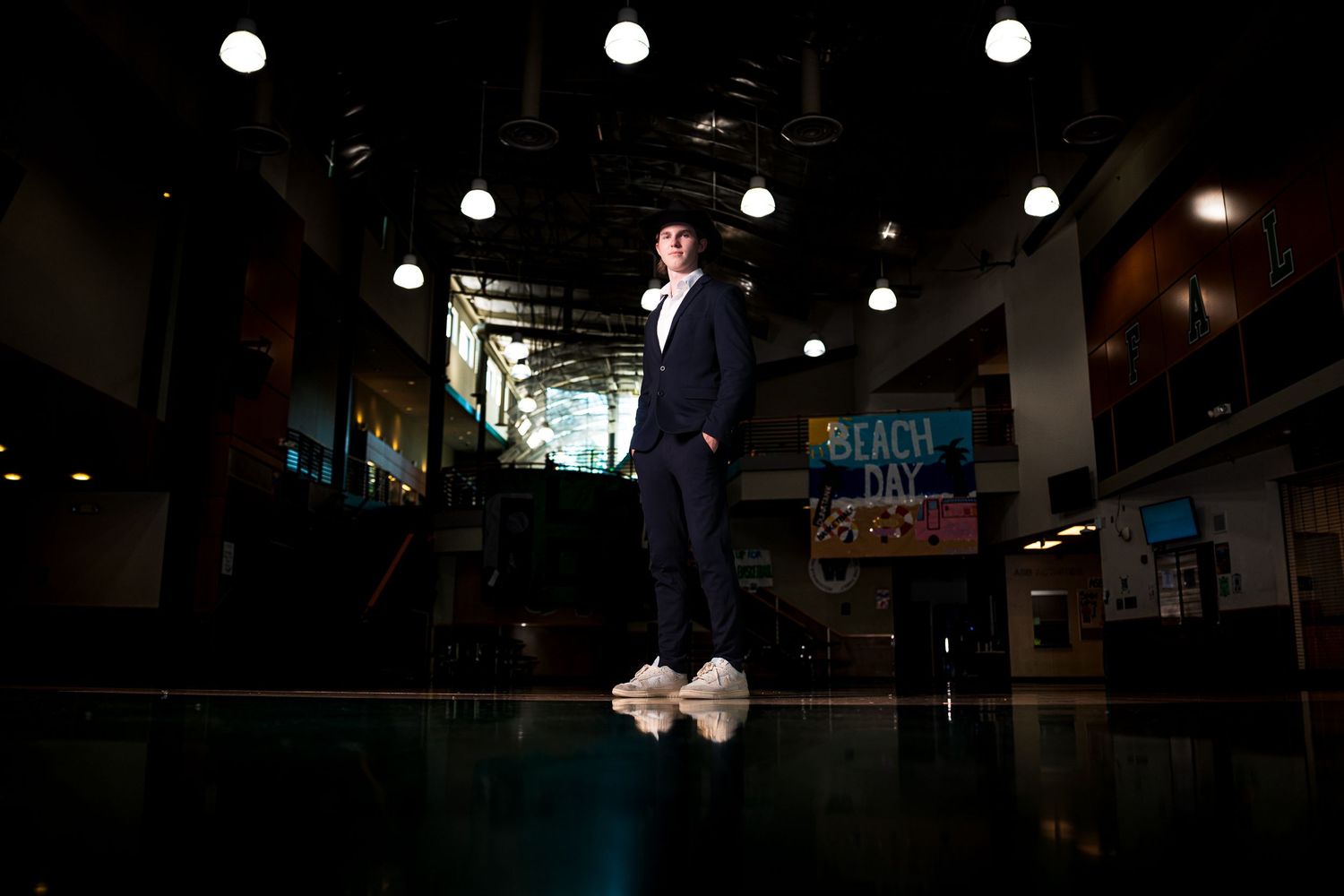 A person in a dark suit stands on a reflective floor under dramatic overhead lighting in an indoor venue.