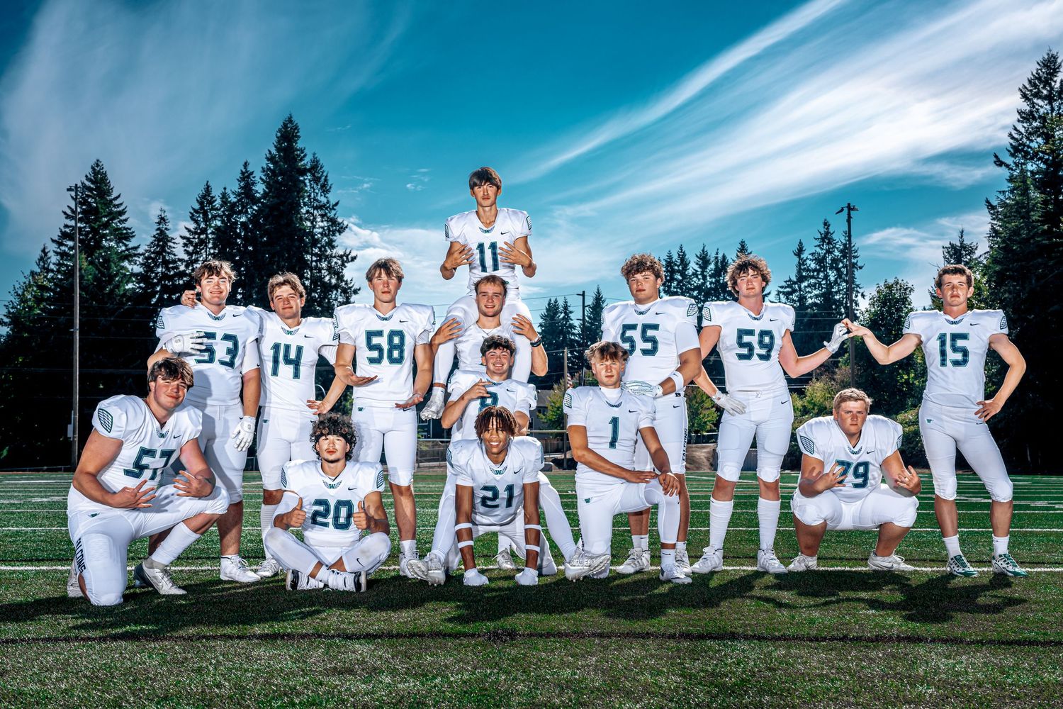 A baseball team poses for a creative panoramic photo lying down in the grass on a sunny day.