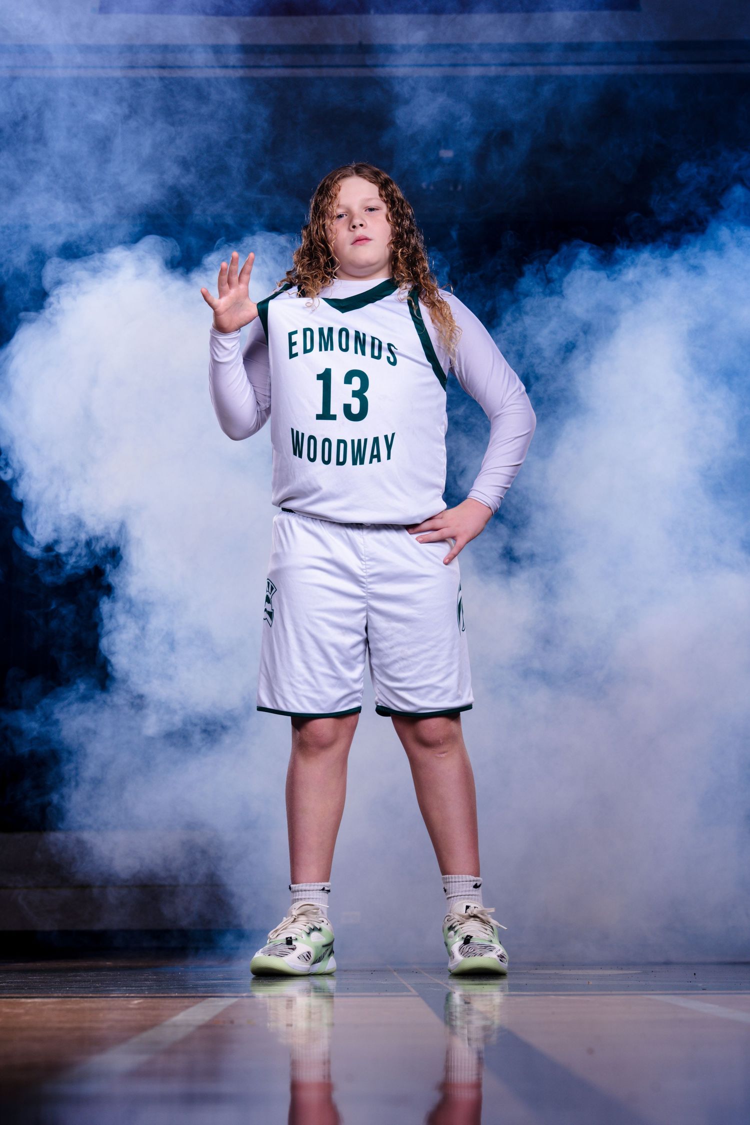 Basketball player in white uniform poses in dramatic smoke effect on dark court.